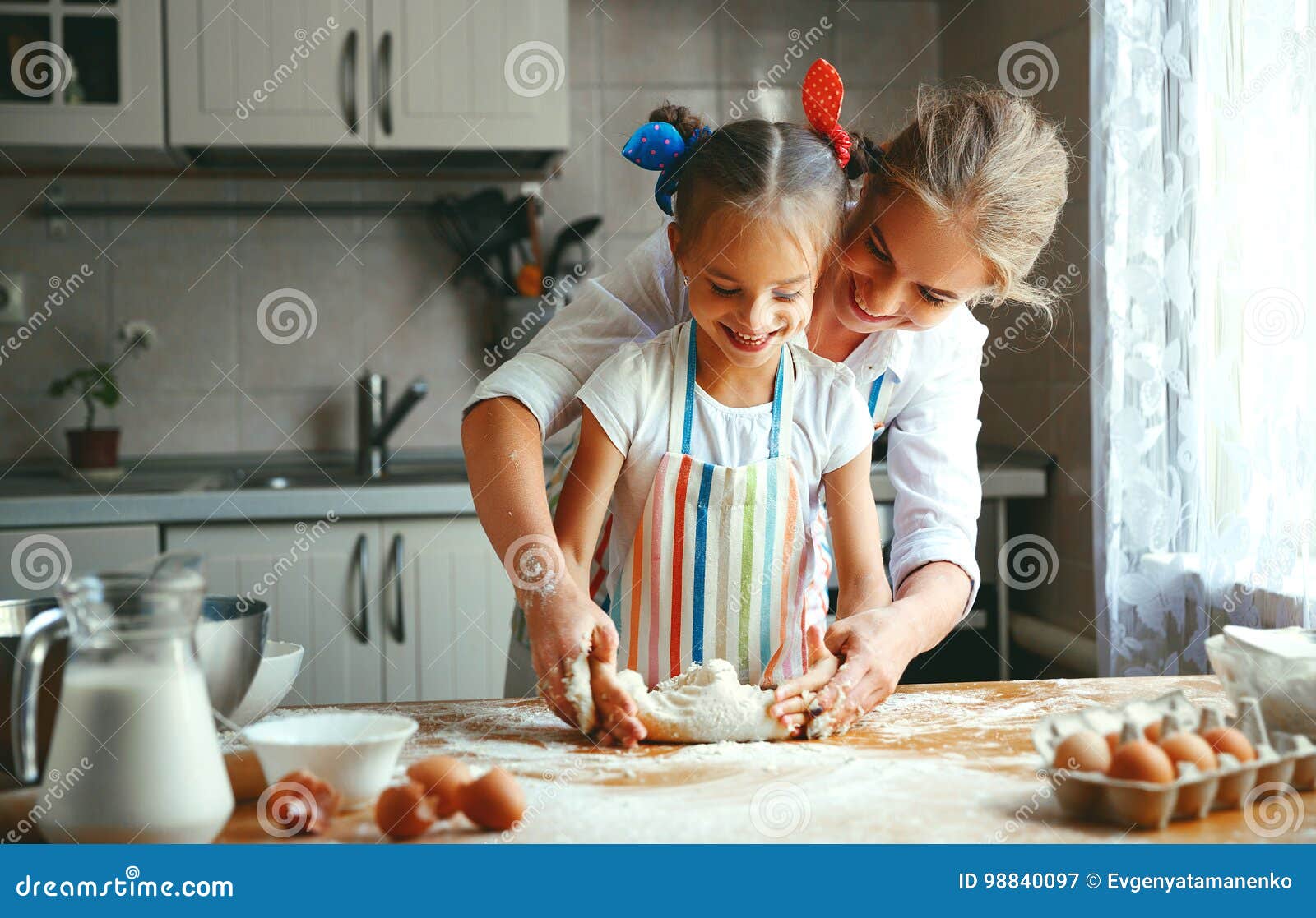 La mère et la fille heureuses de famille font la pâte cuire au four de malaxage dans la cuisine. La mère de famille et la fille heureuses d'enfant font la pâte cuire au four de malaxage dans la cuisine