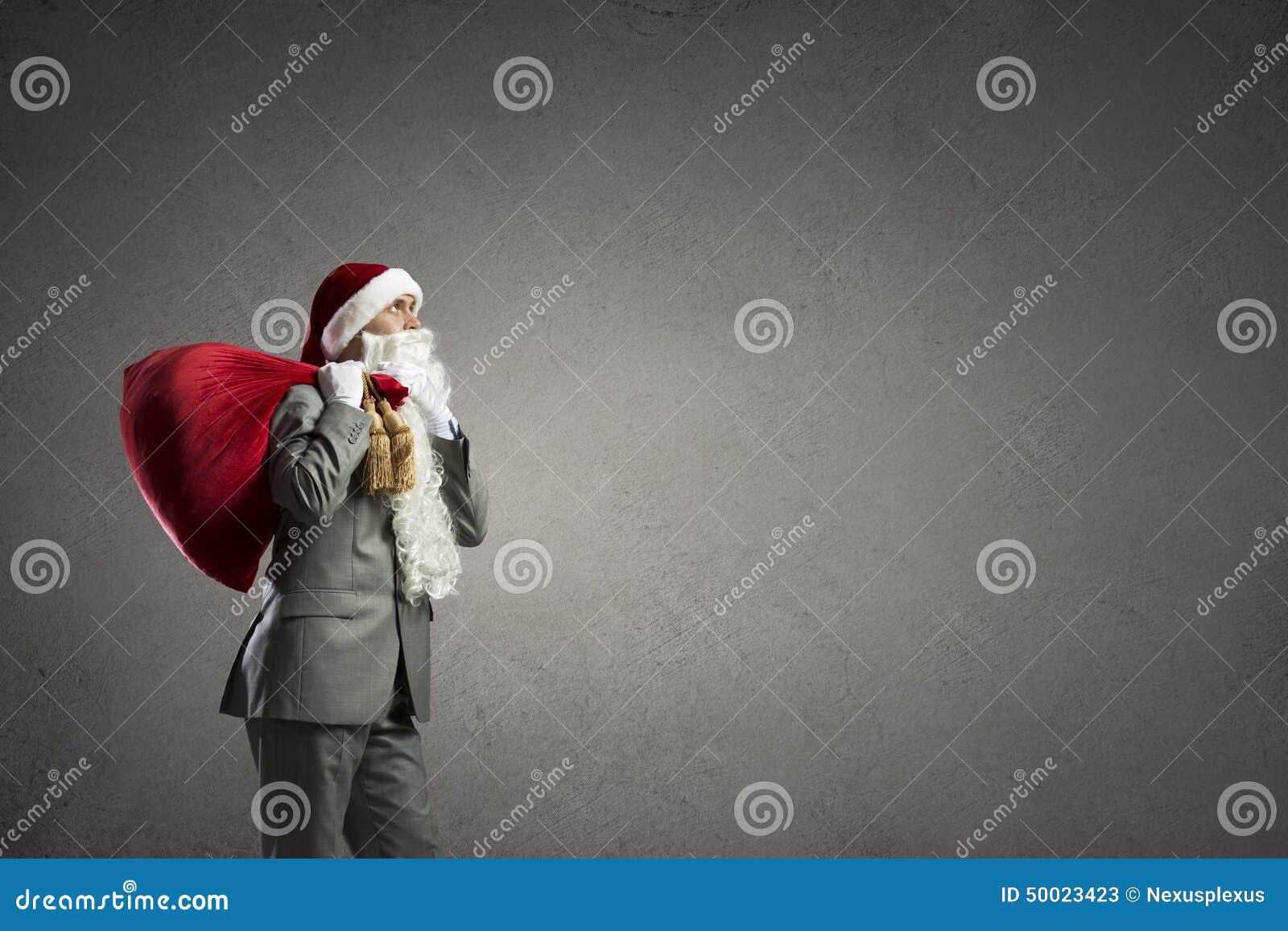¡La Navidad está viniendo!. Hombre de negocios en el sombrero de Papá Noel con del regalo del bolso la parte posterior roja detrás
