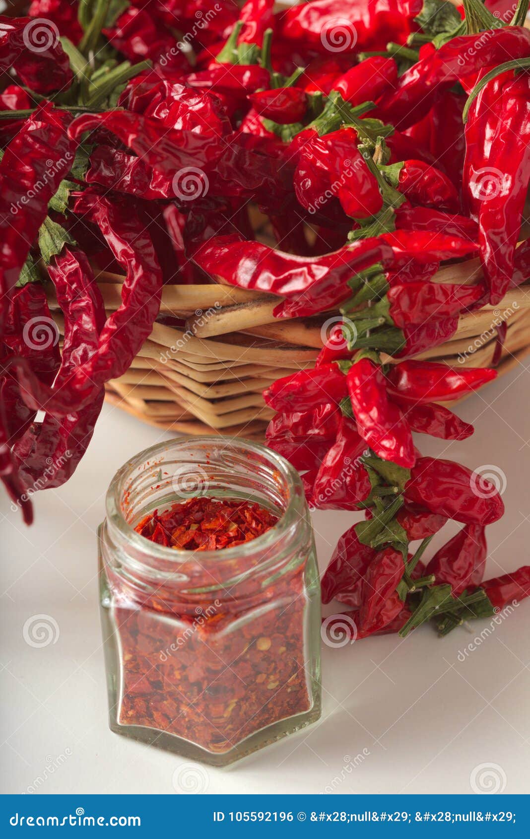 La pimienta roja picante molió en el tarro de cristal, con pimientas secadas sanas en la cesta, en el fondo blanco