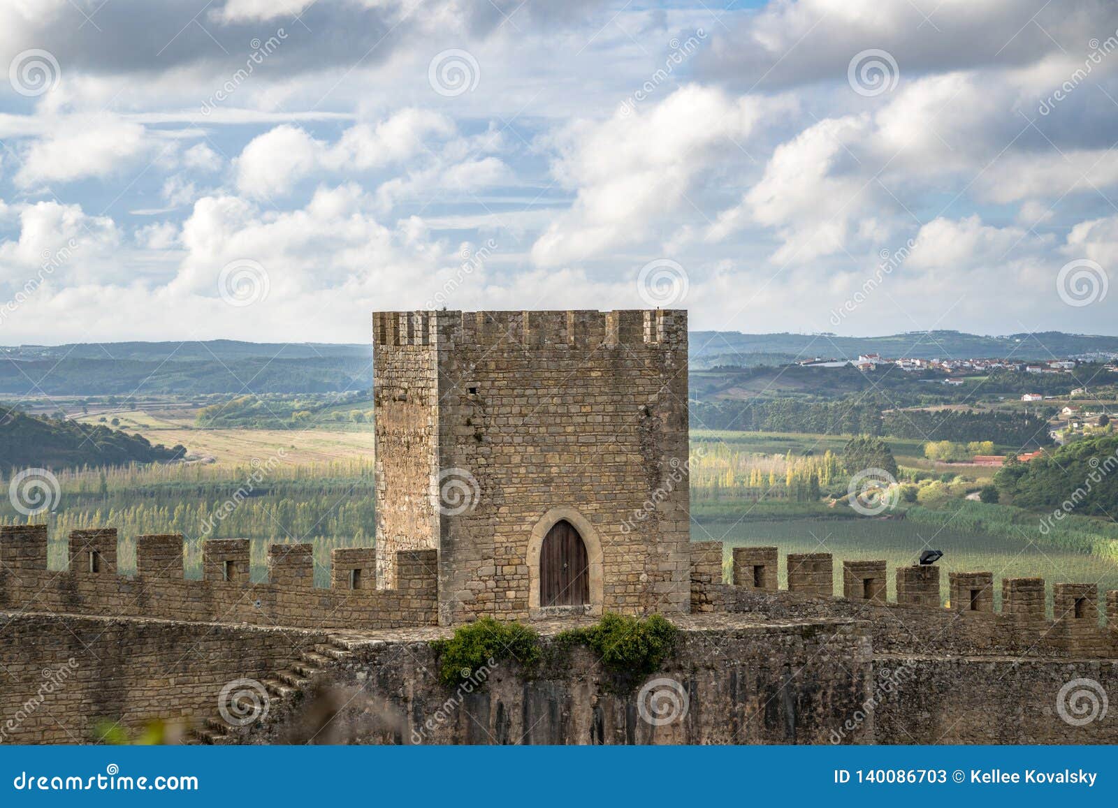 La tour et les murs en pierre médiévaux de château se ferment avec le paysage et le ciel bleu. Tour et murs médiévaux de château avec les étapes et les créneaux en pierre de la défense Vue de jour ensoleillée avec le fond luxuriant de paysage, le ciel bleu avec les nuages gonflés et les couleurs chaudes de ce point de repère portugais européen Tour carrée avec la porte arquée en bois