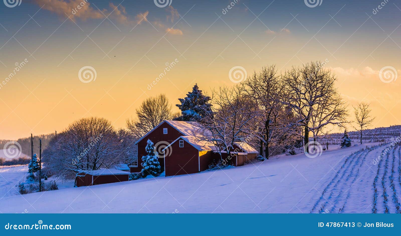 La vue d'hiver d'une grange sur une neige a couvert le champ de ferme au coucher du soleil, dedans. La vue d'hiver d'une grange sur une neige a couvert le champ de ferme au coucher du soleil, dans le comté de York rural, la Pennsylvanie