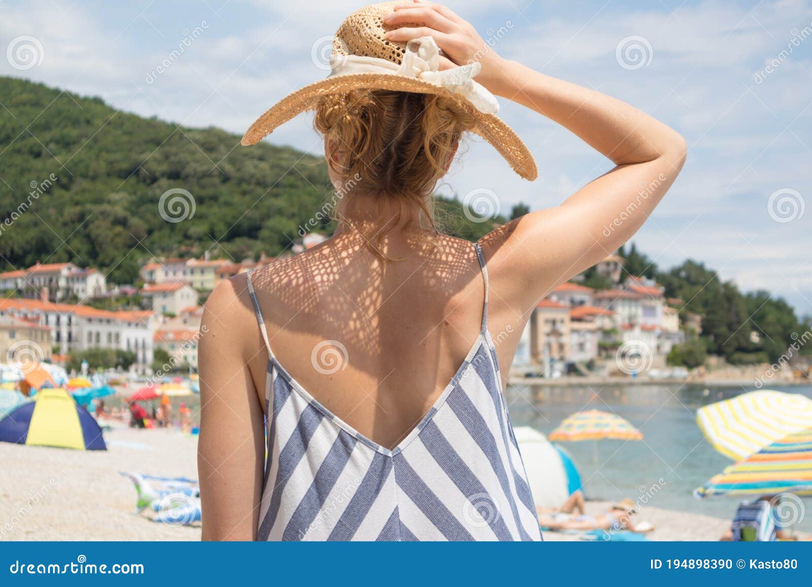 lady wearing striped summer dress and straw hat relaxing on vaction enjoying view over beach at moscenicka draga, istria