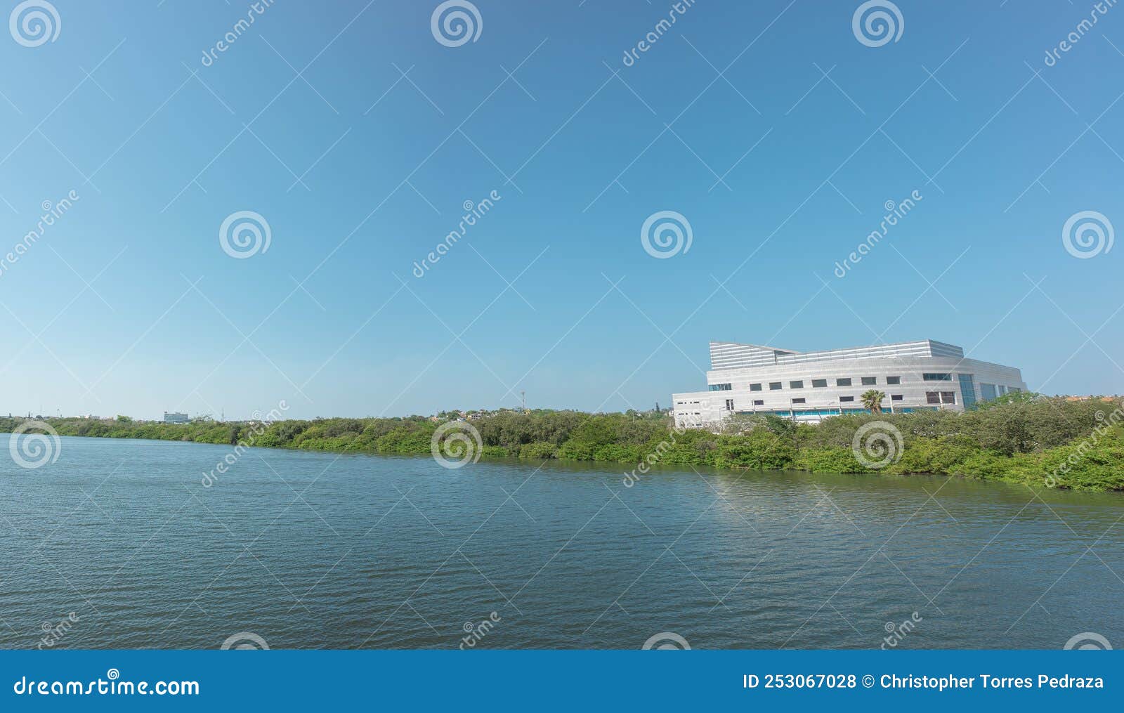 lake with calm water, green trees, blue sky and a building in the background, laguna del carpintero in tampico tamaulipas,