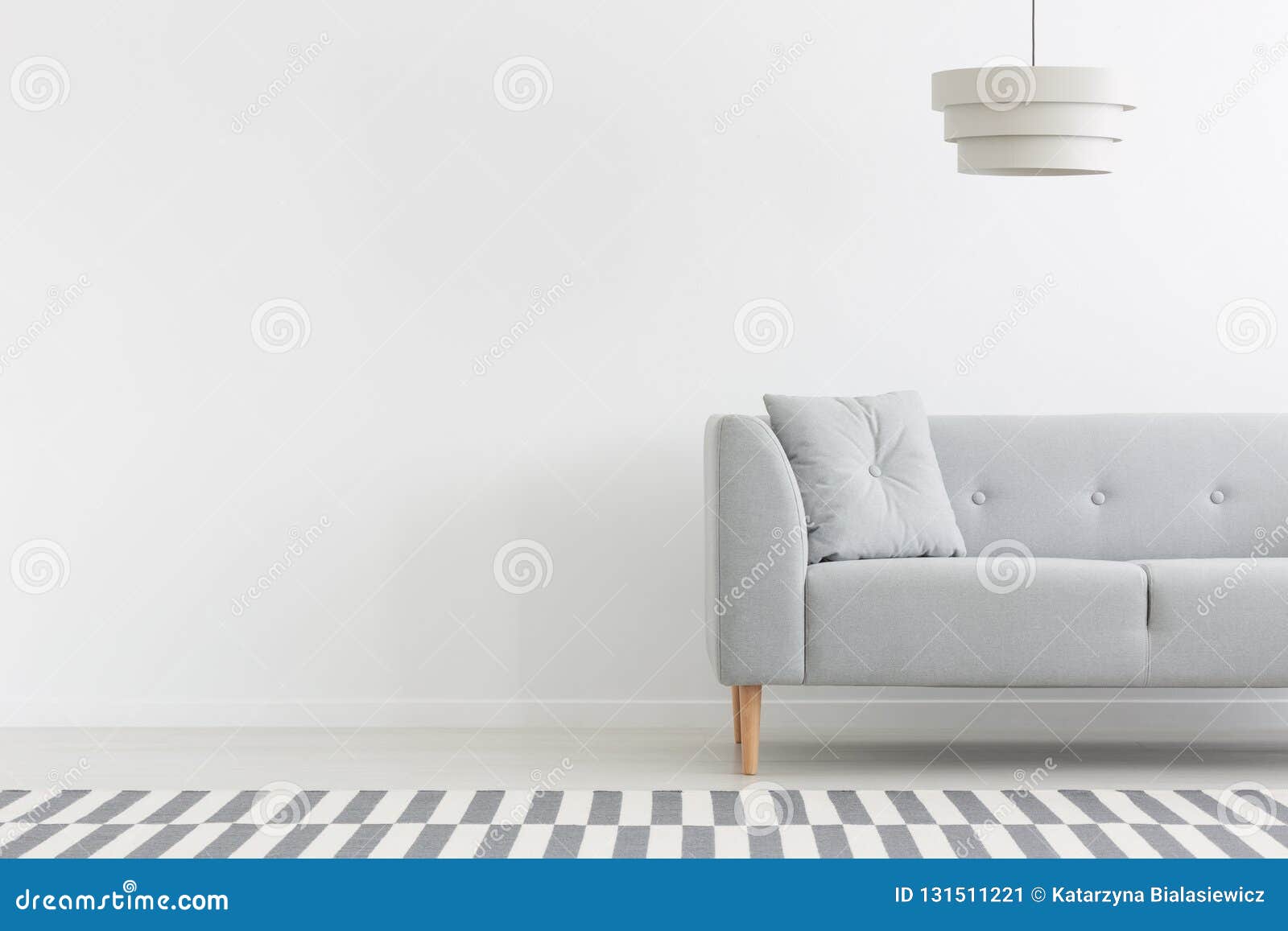 grey couch in white minimal apartment interior with copy space on empty wall. real photo