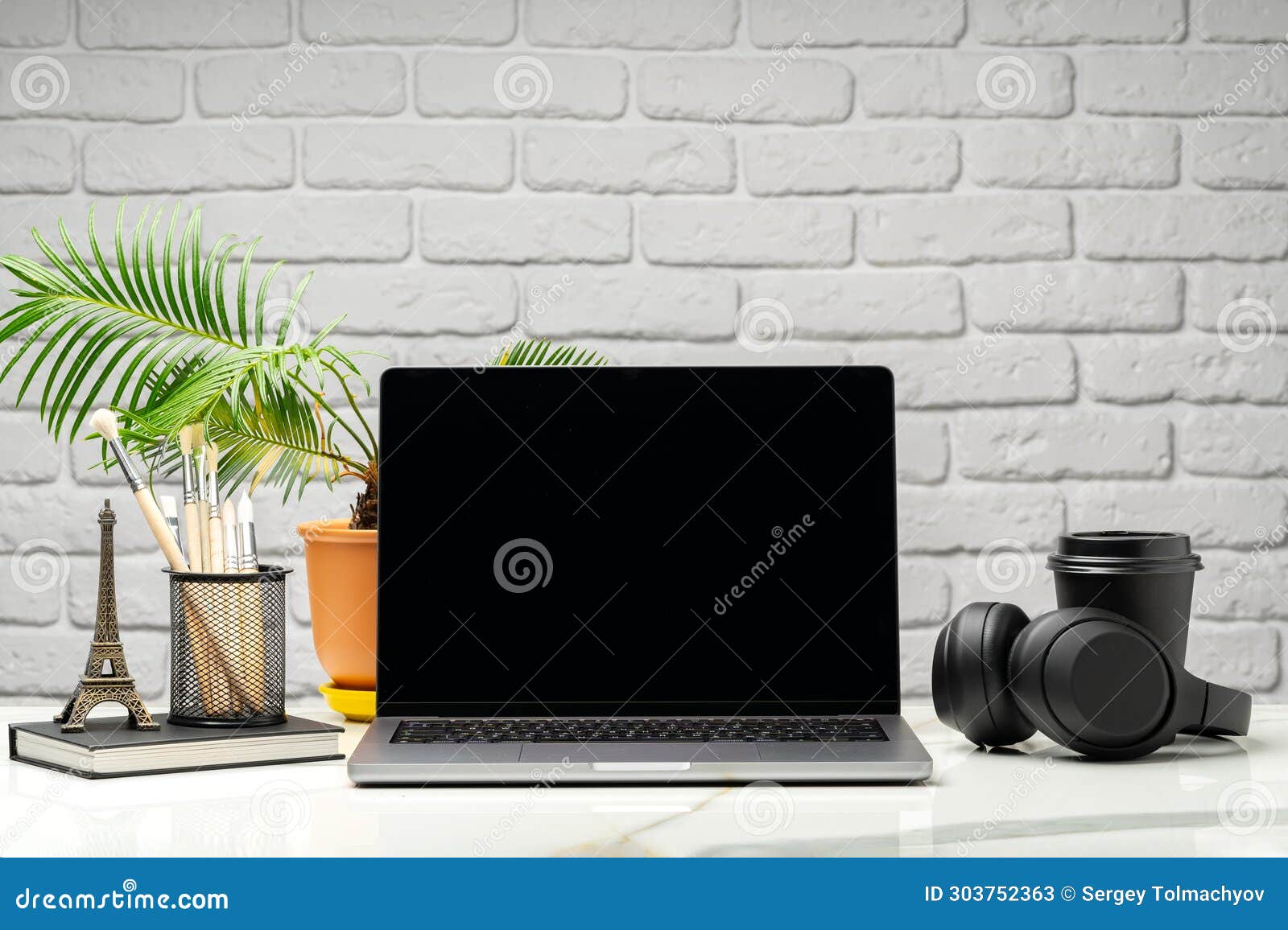 Laptop with Black Screen on Desk Against White Brick Wall Stock Image