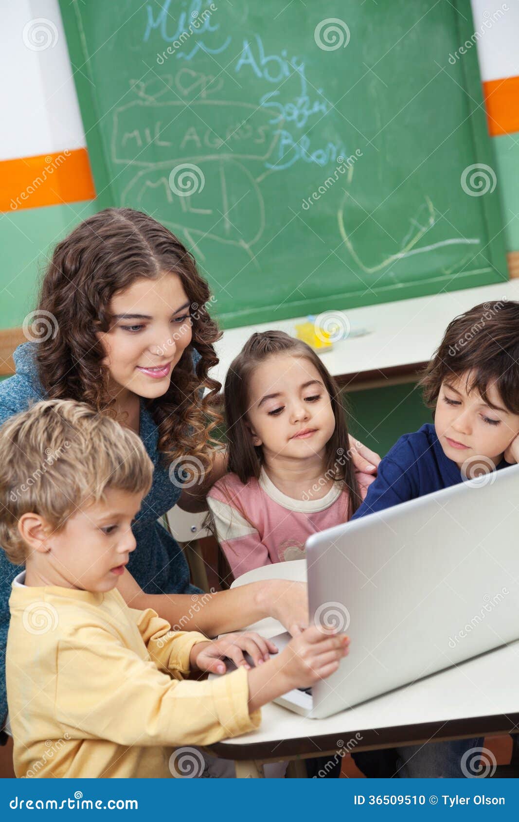 Laptop van leraarsand students using in Klasse. Jonge leraar en studenten die laptop met behulp van bij bureau in klasse