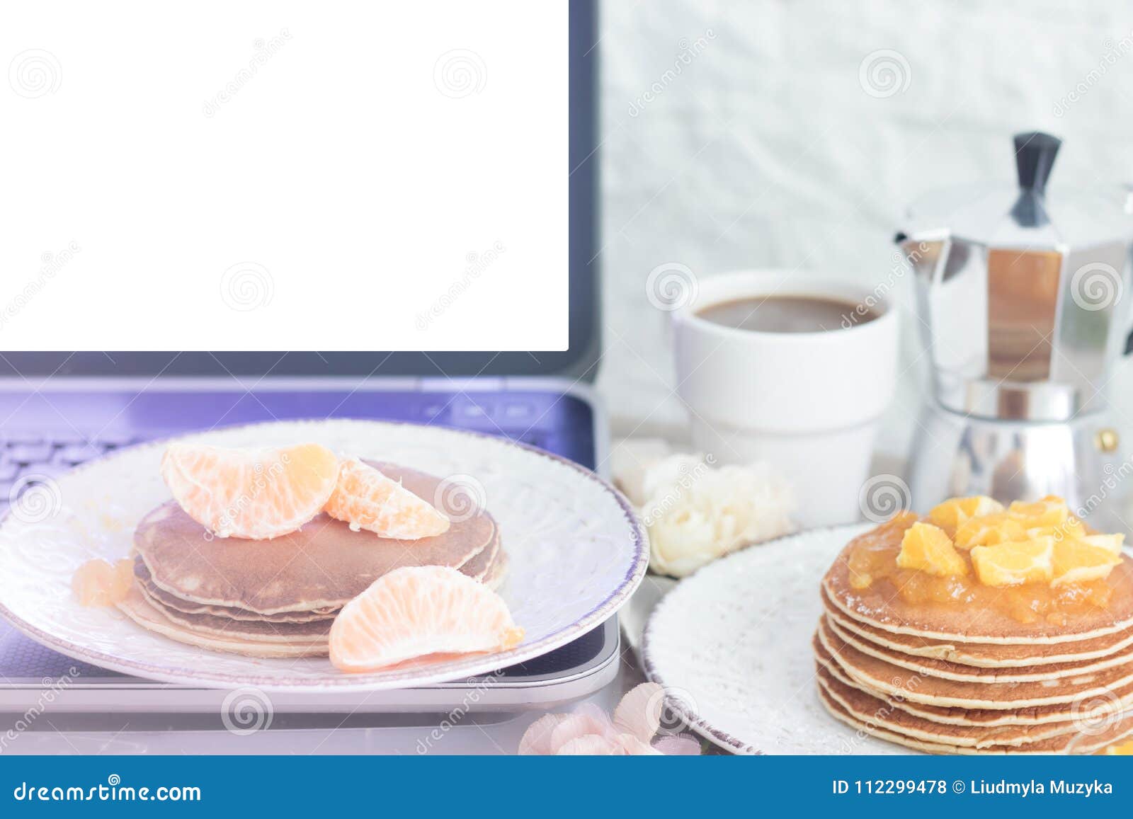workplace. laptop with blank screen on table with breakfast: pancakes and coffee. front view. copy space