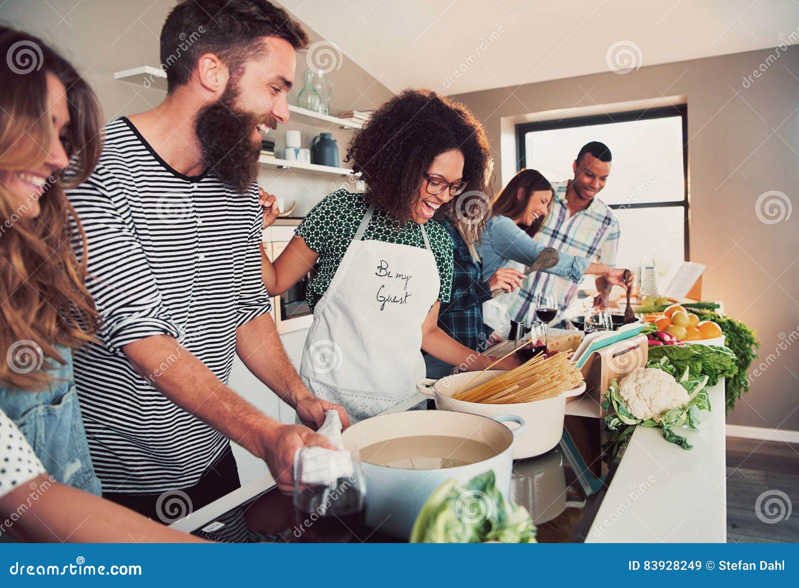 large group of six friends cooking pasta at table