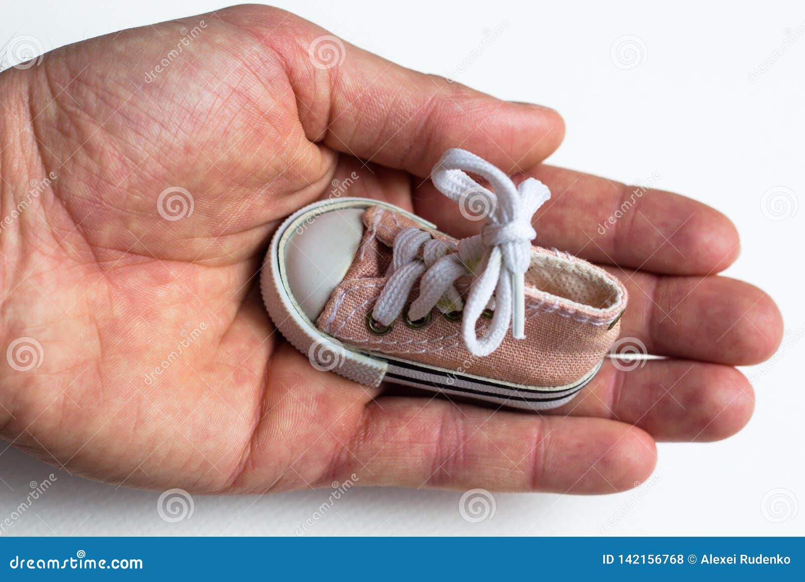 in a large and strong male hand is a small children`s shoes. on shoes tied with a bow bow.