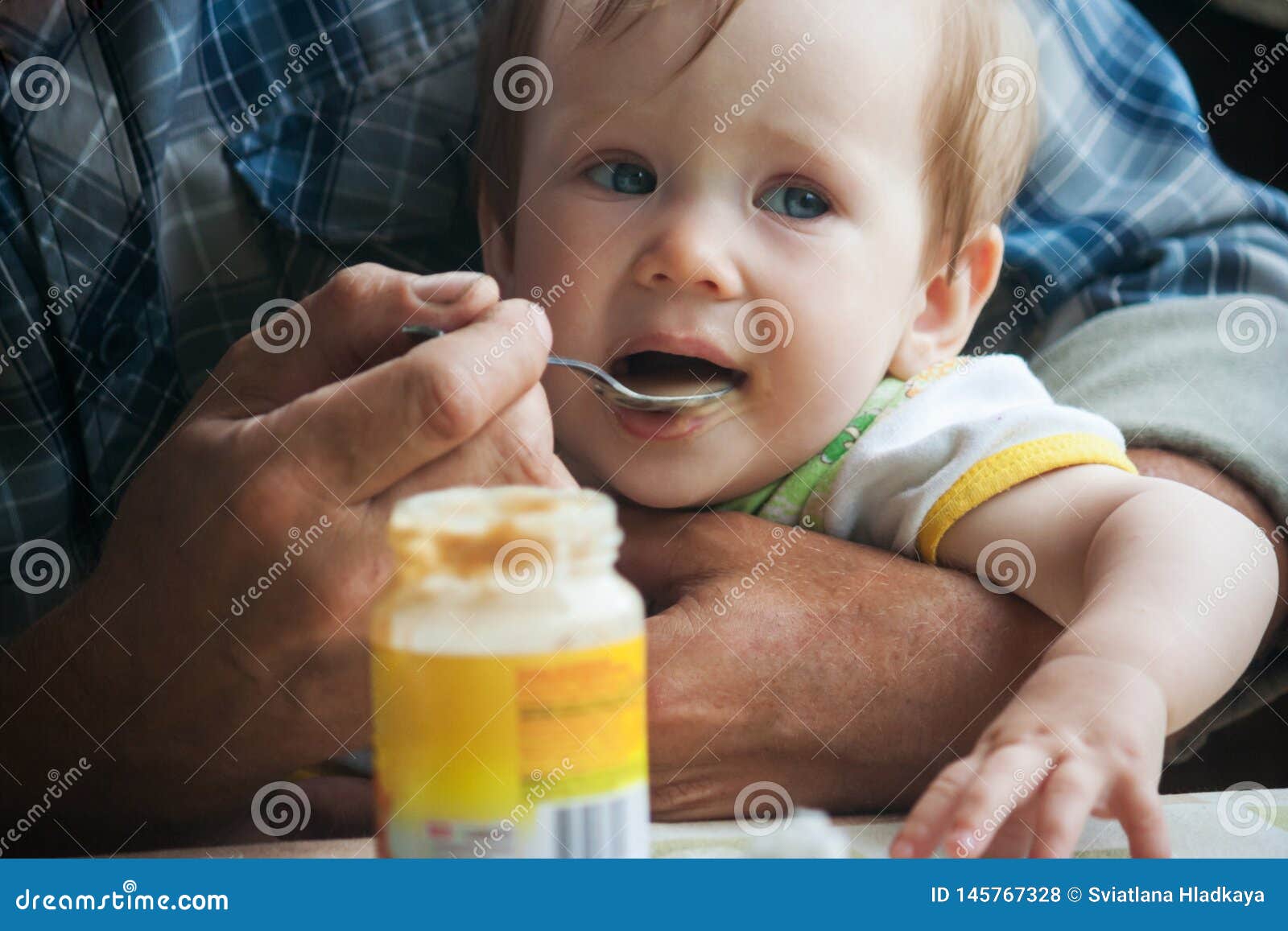 Un pequeño bebé se sienta en los brazos de su abuelo y come un puré de la fruta con una cuchara Introducción de comidas complementarias en un niño Las manos ásperas grandes apoyan suavemente al bebé y se alimentan con una cuchara