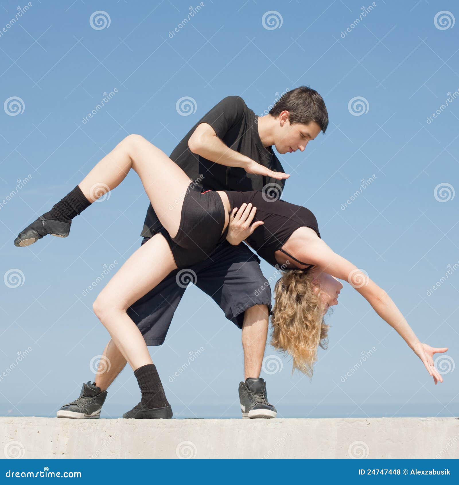 Late teenagers dancing outdoors. Teenage couple in black are dancing on background of sky