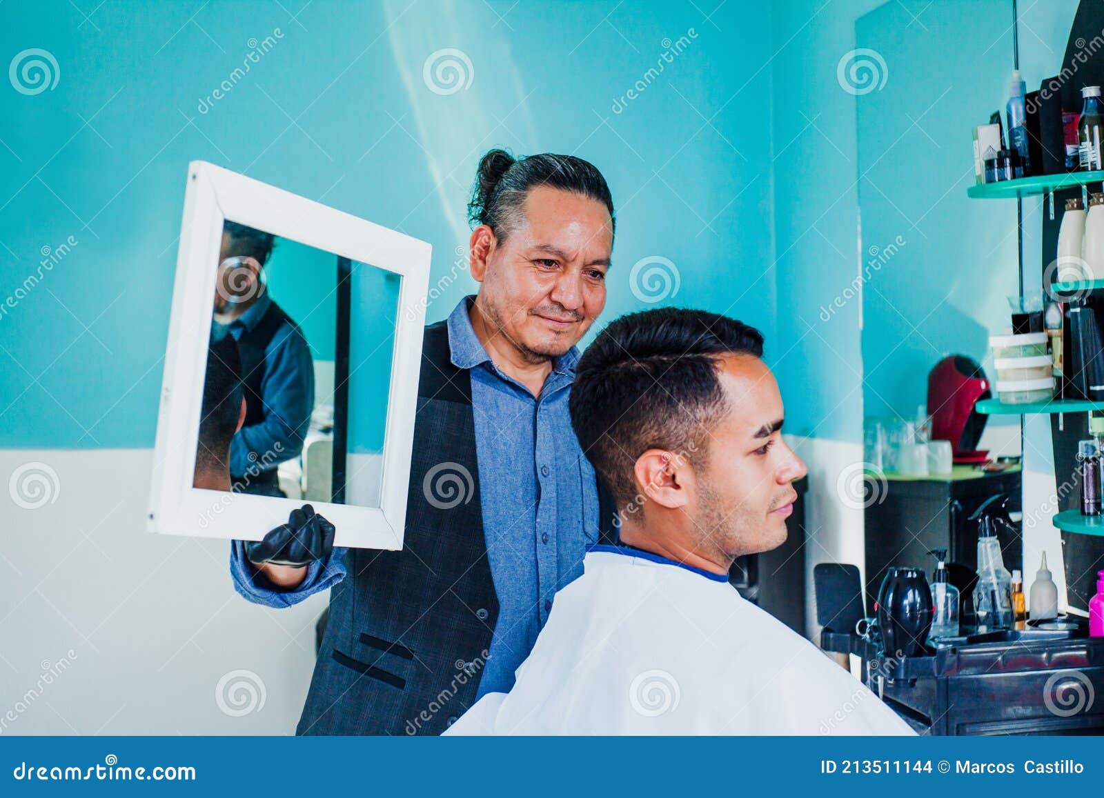 latin man stylist cutting hair to a client and holding a mirror in a barber shop in mexico