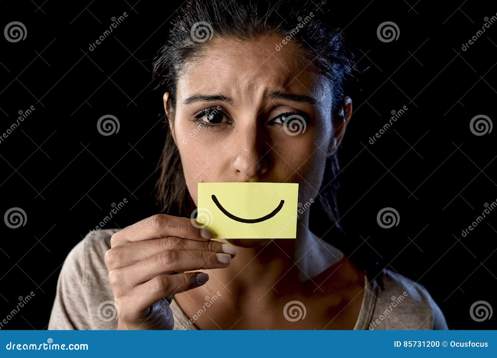 latin sad depressed latin girl holding paper hiding her mouth behind fake drawn smile