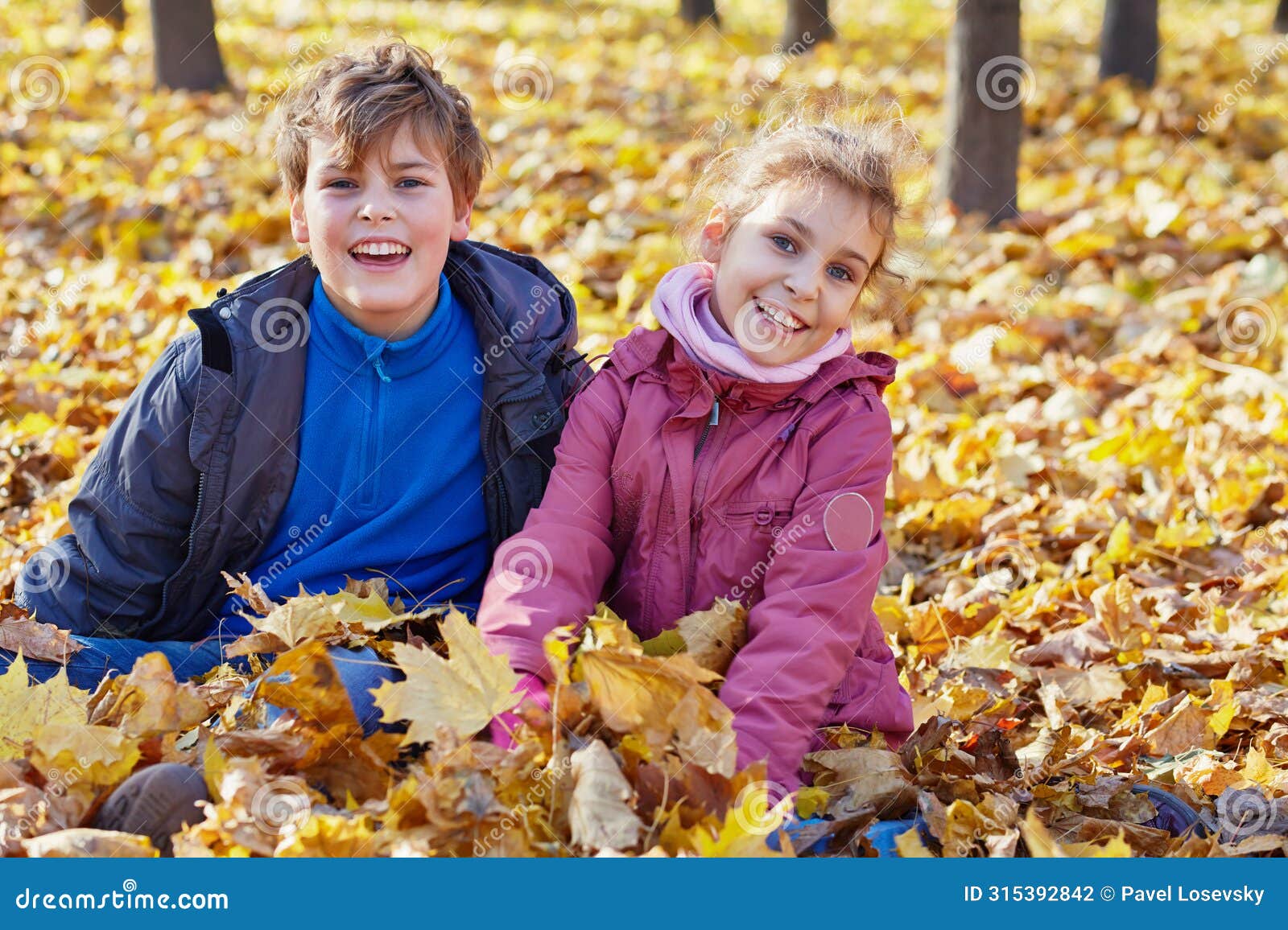 laughing boy and girl sit on ground in drift of