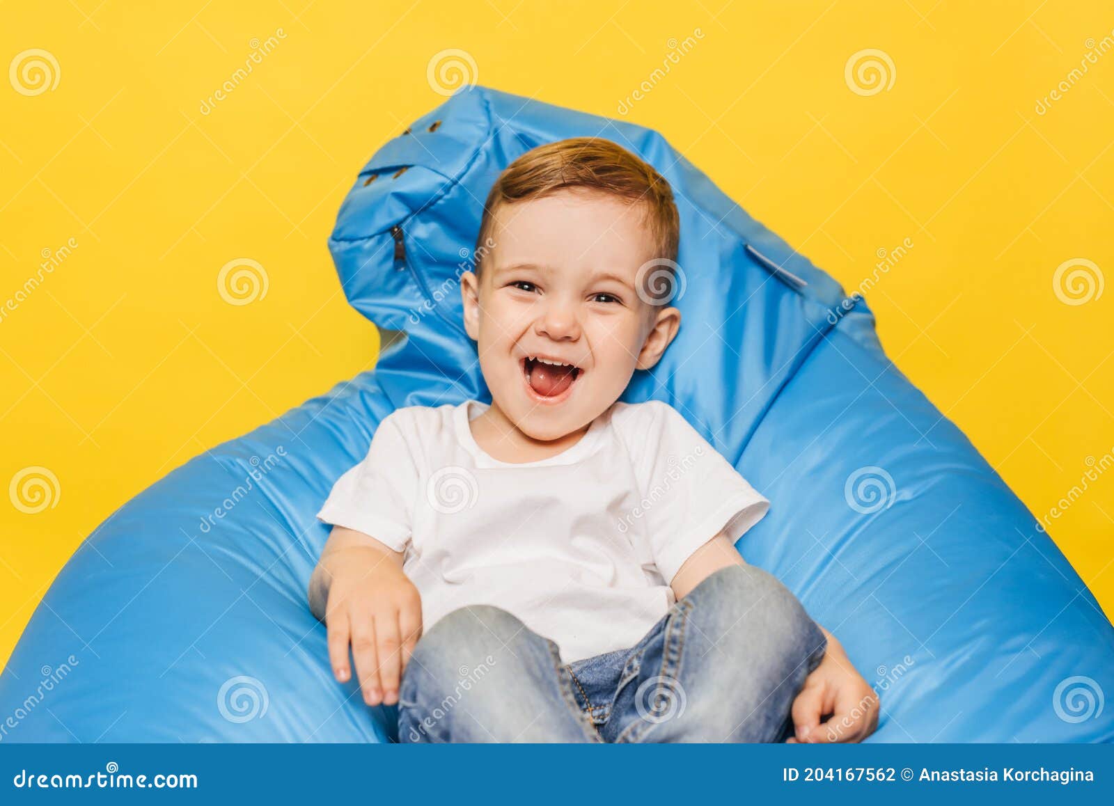 Laughing Little Boy on a Yellow Background Sitting in a Blue Chair ...