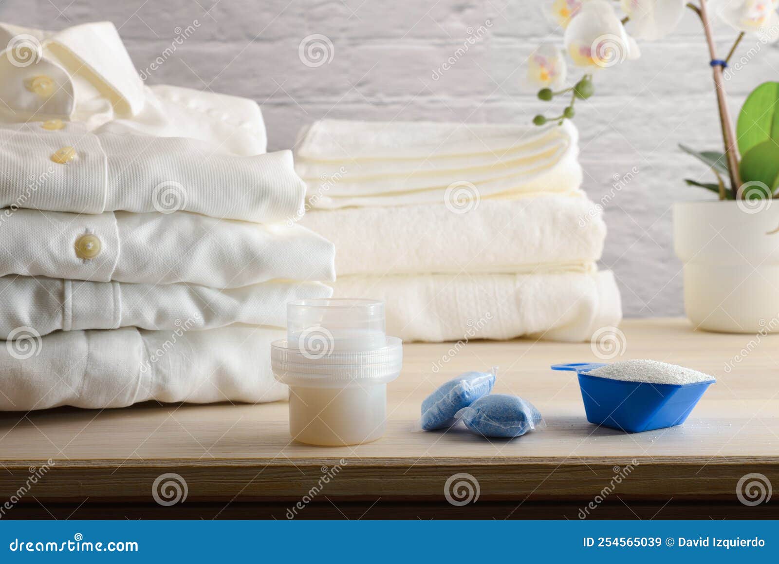 Laundry Detergents on Wooden Table with Freshly Washed Folded Clothes