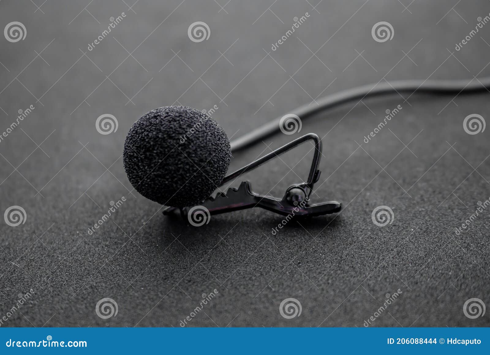 lavalier or lapel microphone on a black surface, very close-up. the details of the grip clip or bra and the sponge against the