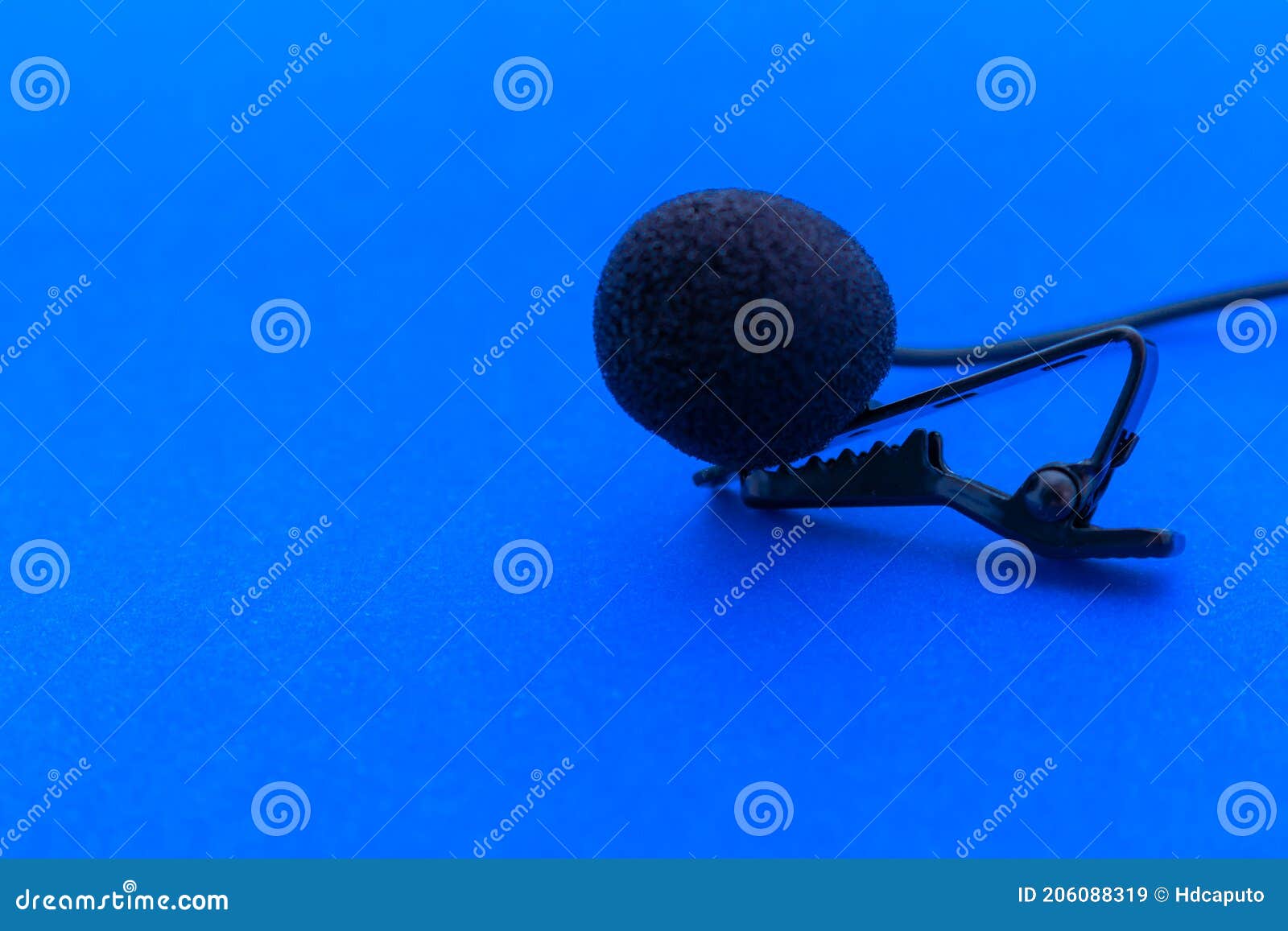 lavalier or lapel microphone on a blue surface, very close-up. the details of the grip clip or bra and the sponge against the wind