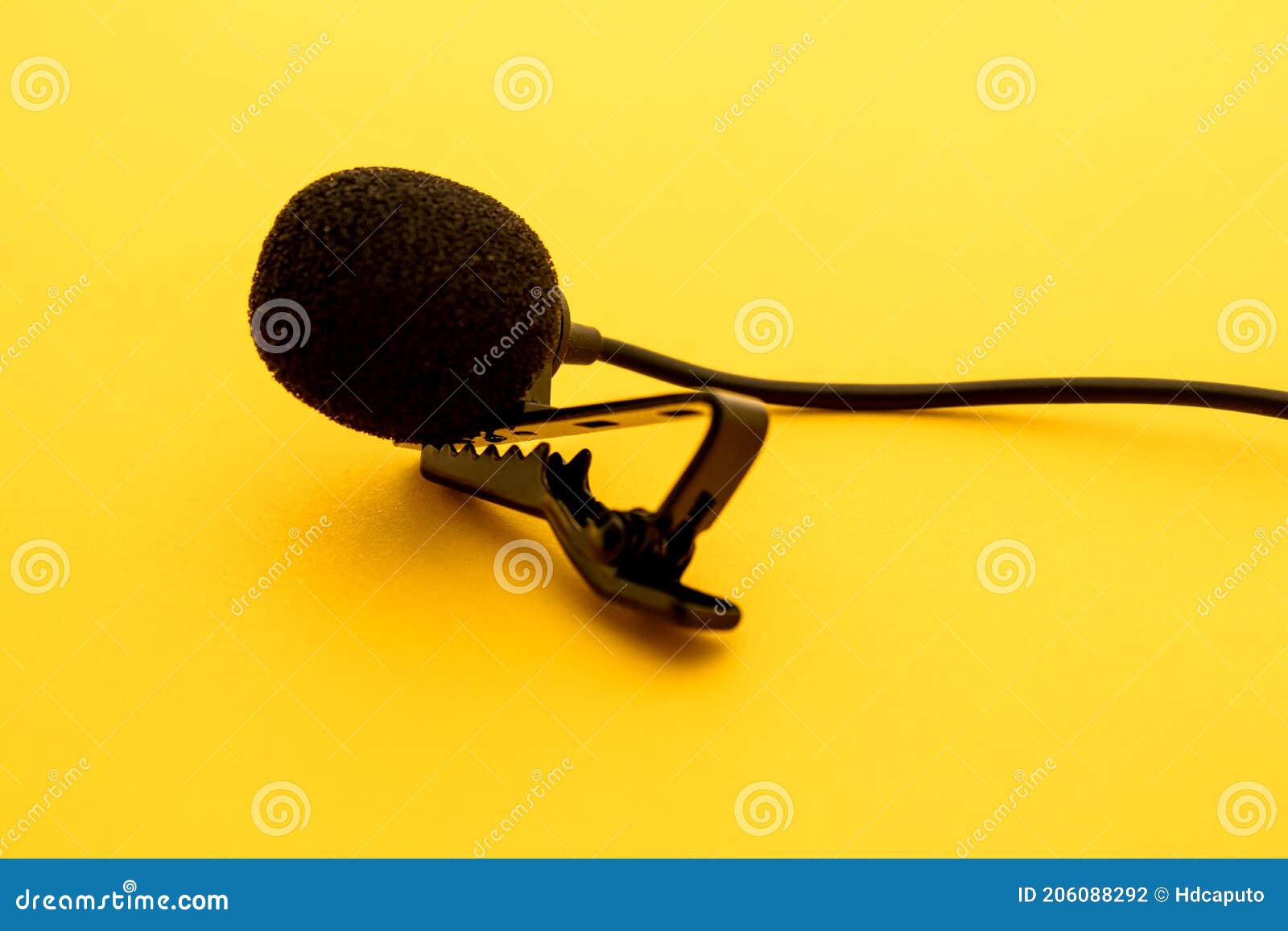 lavalier or lapel microphone on a yellow surface, very close-up. the details of the grip clip or bra and the sponge against the