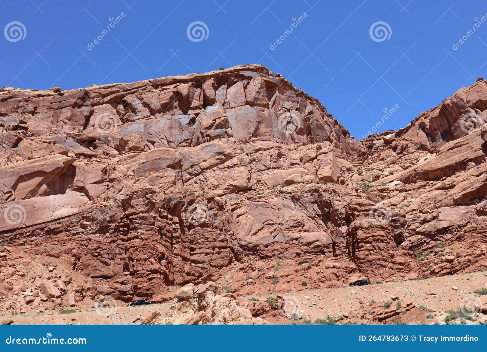 layers of entrada sandstone behind the road leading into arches national park contrasted against a clear, blue sky