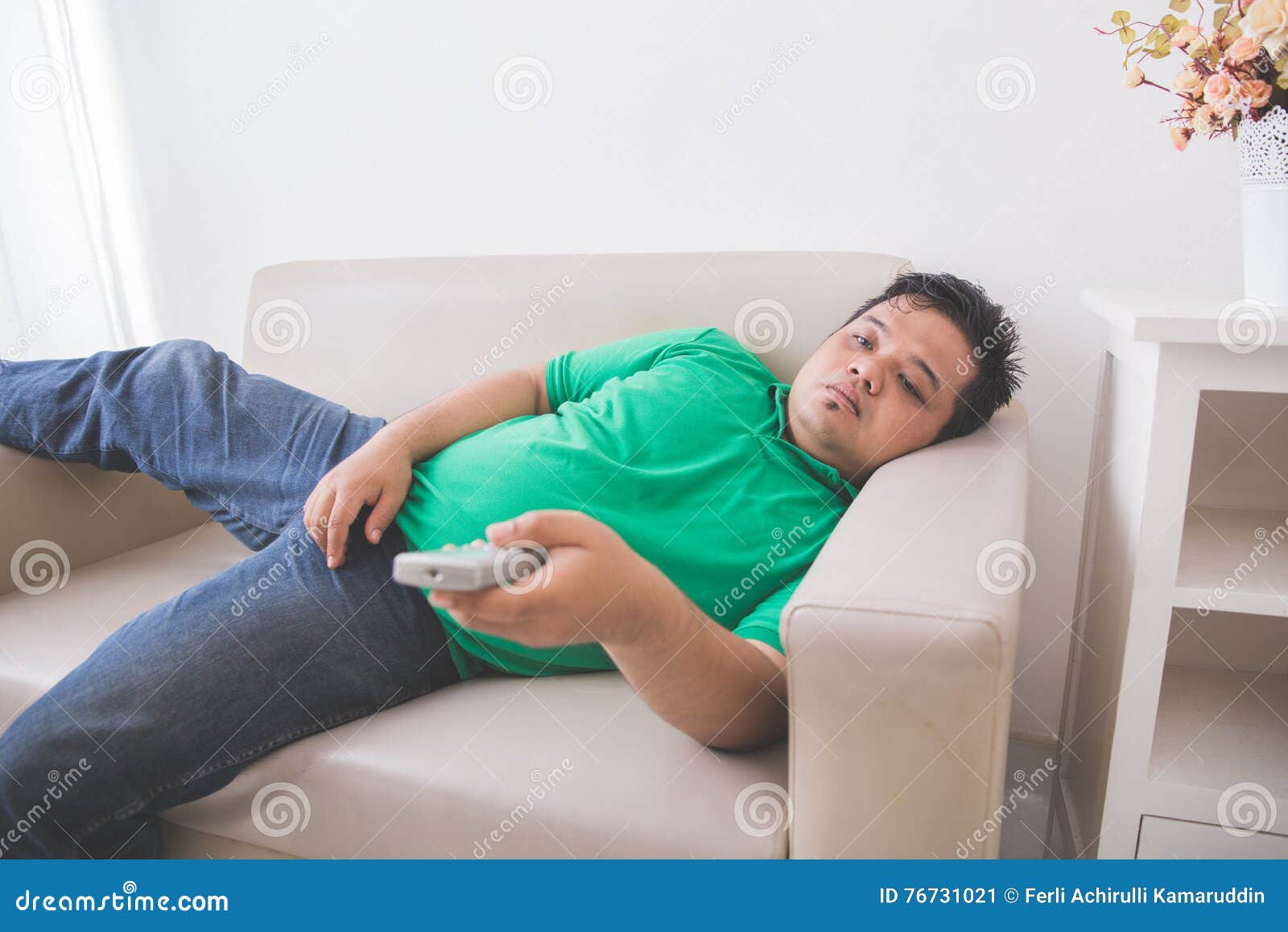 lazy fat obese man laying on the couch and watching tv