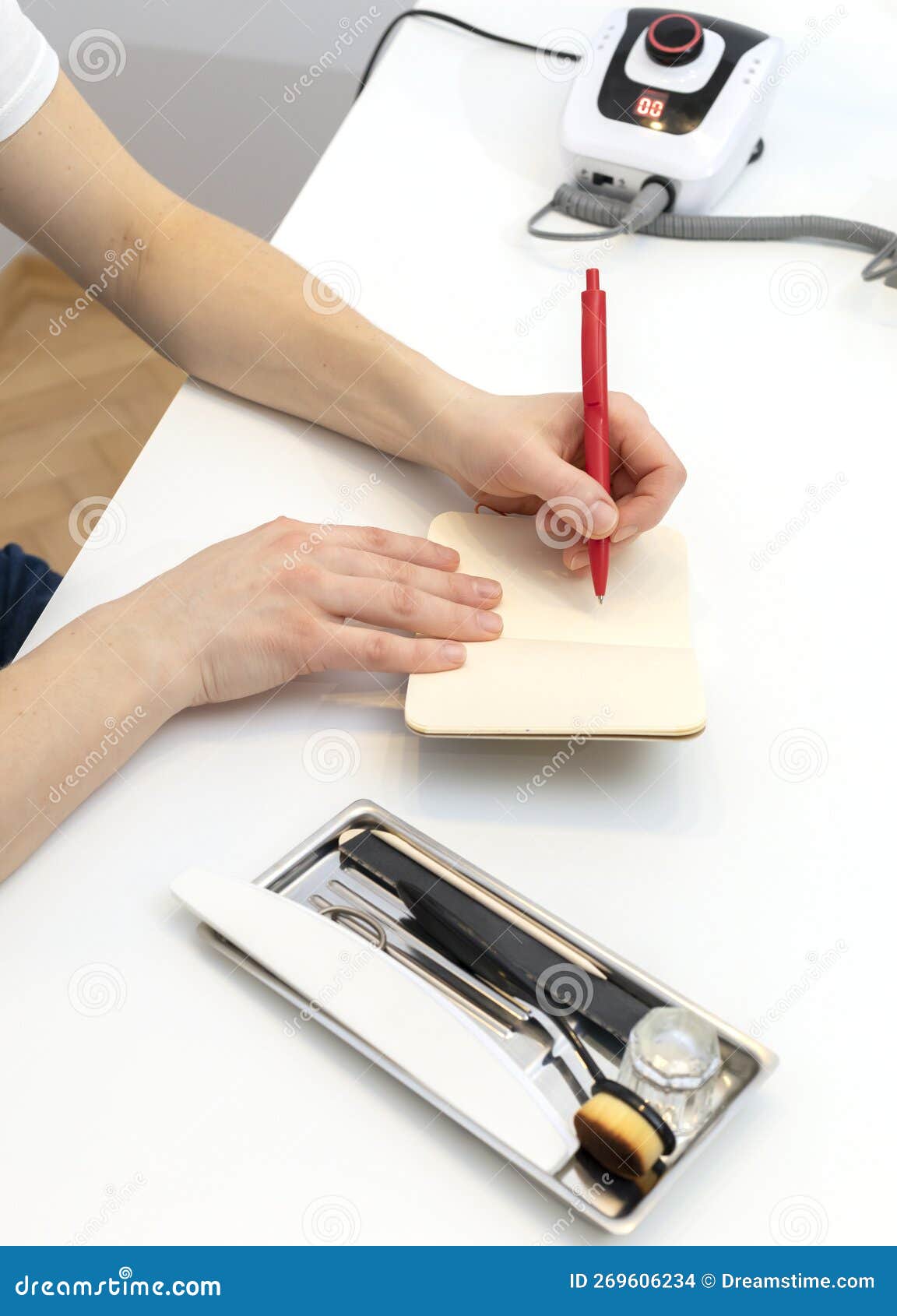 left handed nail master makes notes in notebook with pen, sitting at workstation