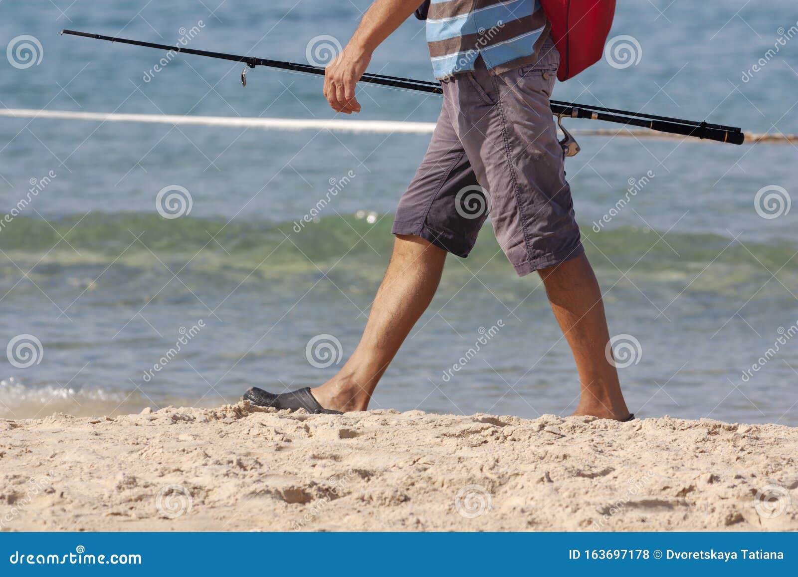 A Fisherman Walks Along the Beach with a Fishing Rod in His Hand