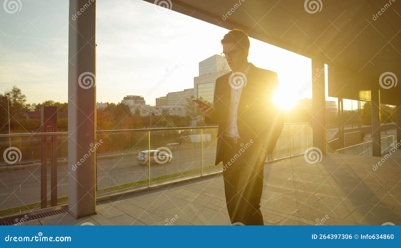 lens flare: young yuppie looks at his smartphone while walking down the street.