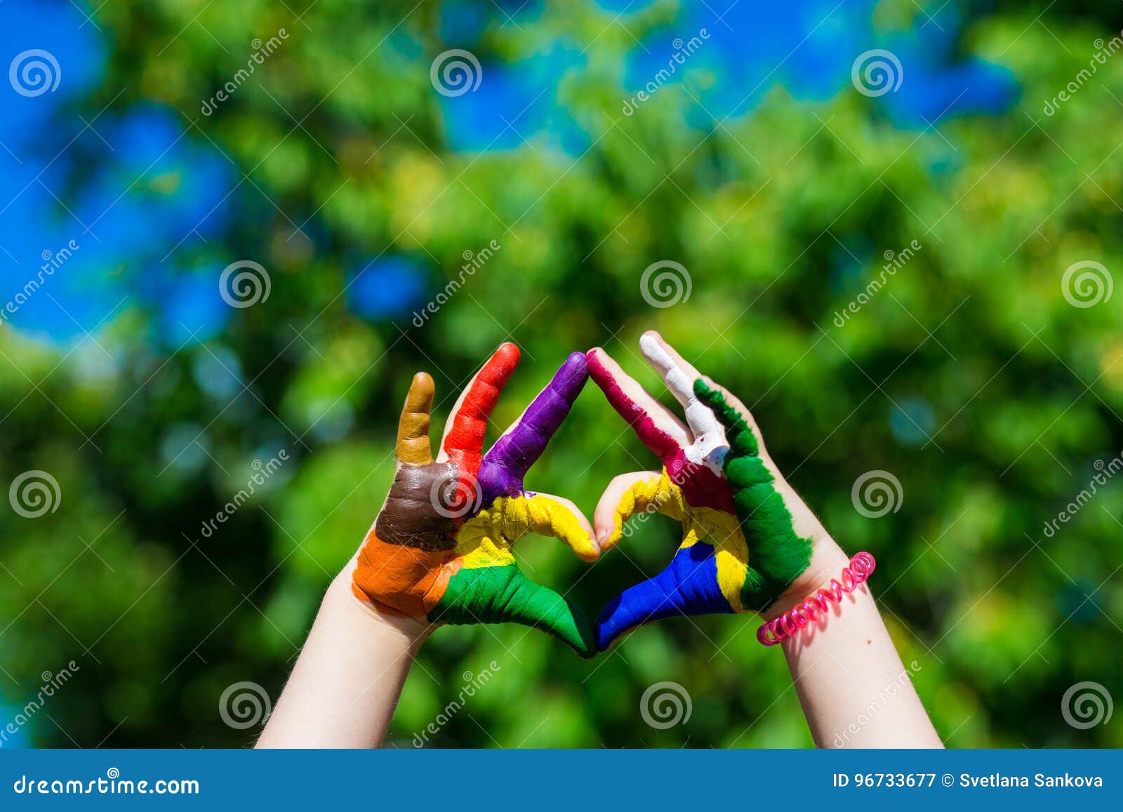 Les mains d'enfants peintes dans des couleurs lumineuses font une forme de coeur sur le fond de nature d'été. Les mains d'enfants peintes dans des couleurs lumineuses font une forme de coeur sur le fond de nature Concept d'art et de peinture