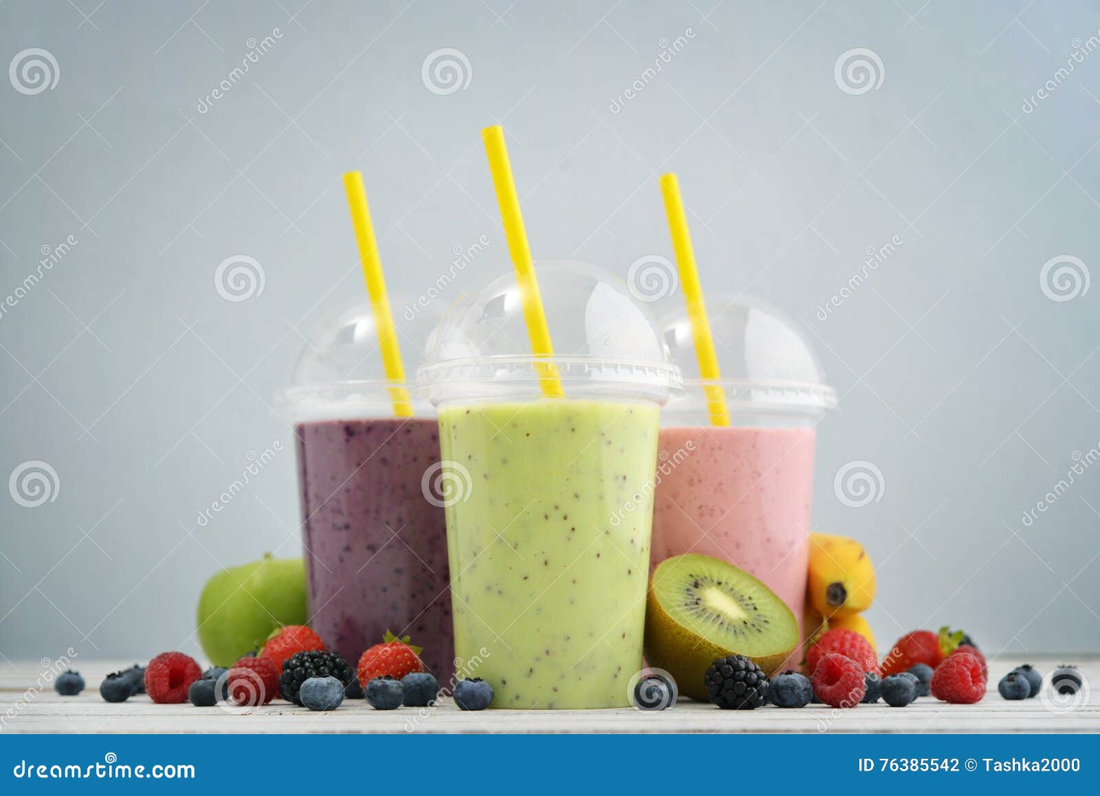 Batidos de fruta em uns copos plásticos com mirtilo, morango, quivi, amora-preta, framboesa e banana no fundo azul Leve embora o conceito das bebidas