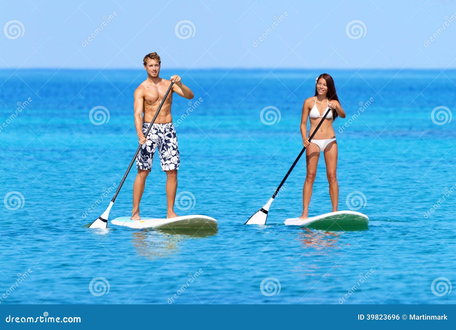 Levántese a la gente de la playa del paddleboard en el tablero de paleta. Coloque a la gente para arriba paddleboarding de la playa encendido se levantan el tablero de paleta, tabla hawaiana del SORBO que practica surf en el mar del océano en las mujeres asiáticas de la raza mixta joven hermosa grande de la isla, de Hawaii y los hombres caucásicos que hacen el deporte acuático.