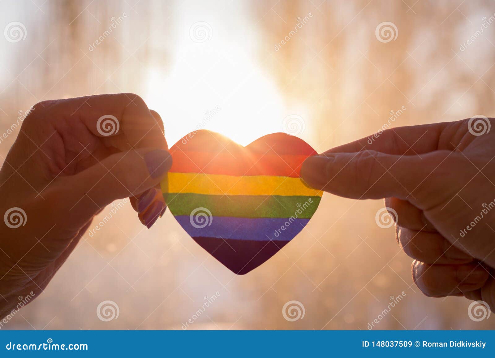 hand holds a heart painted like a lgbt flag