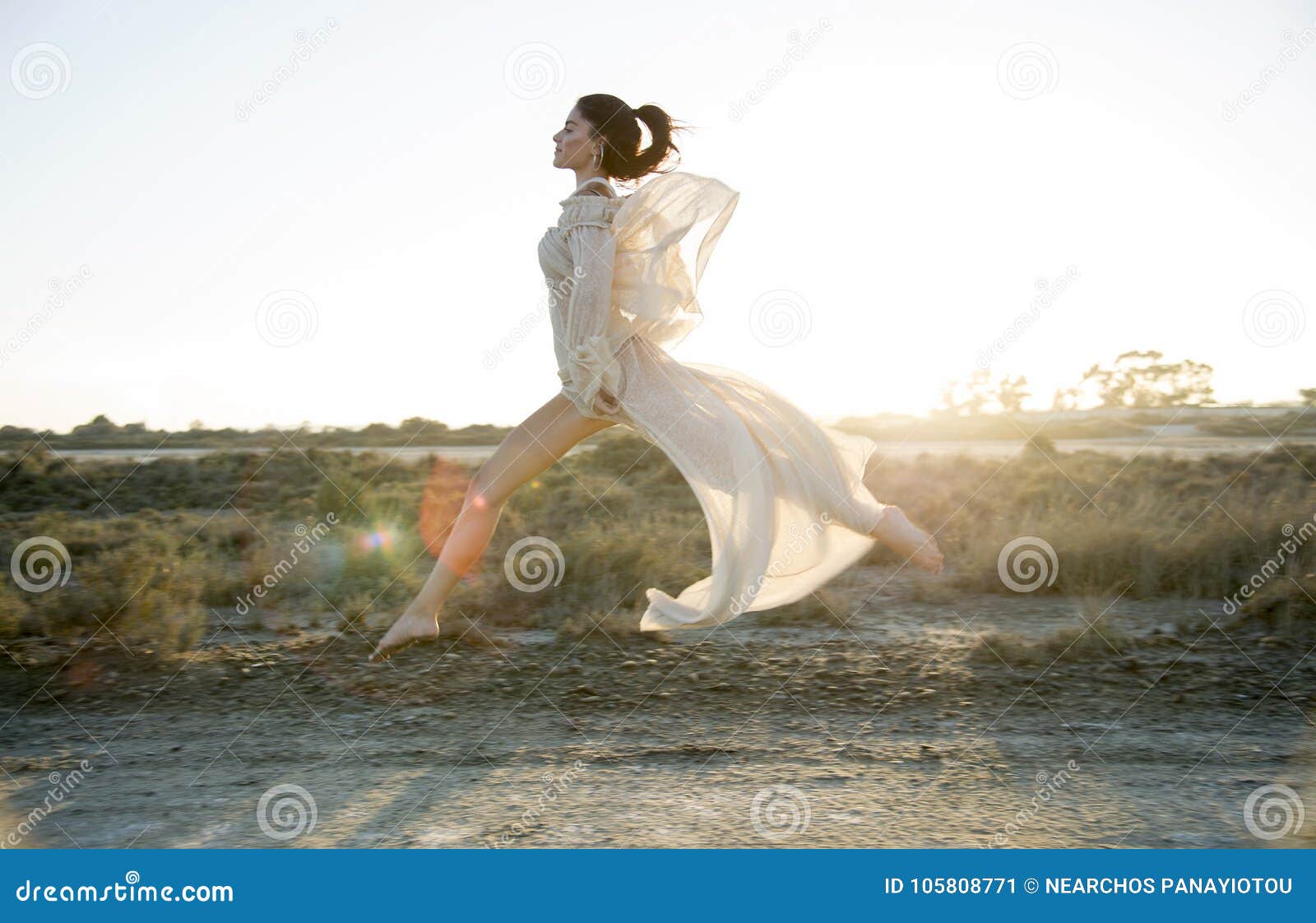 Liberté de la vie. La fille sautant dans le domaine au coucher du soleil portant une robe blanche