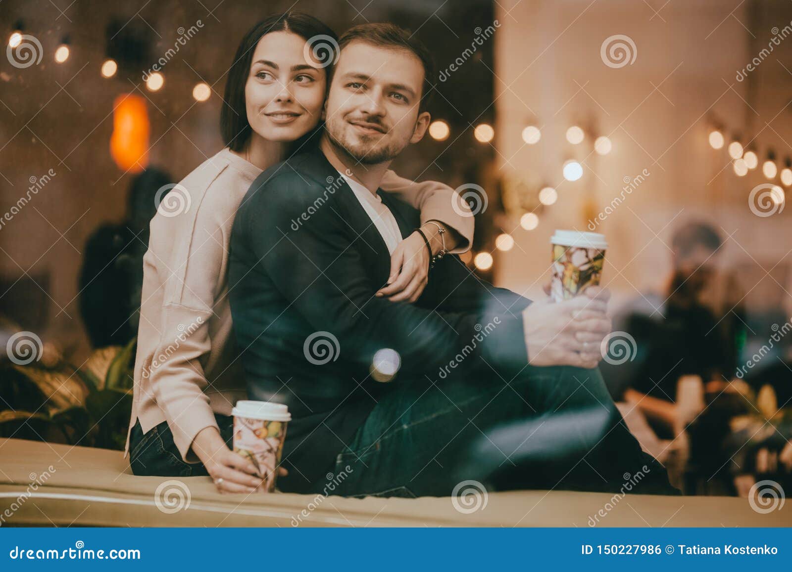 Liebender Kerl und Mädchen sitzen das Umarmen auf dem Fensterbrett in einem romantischen Café