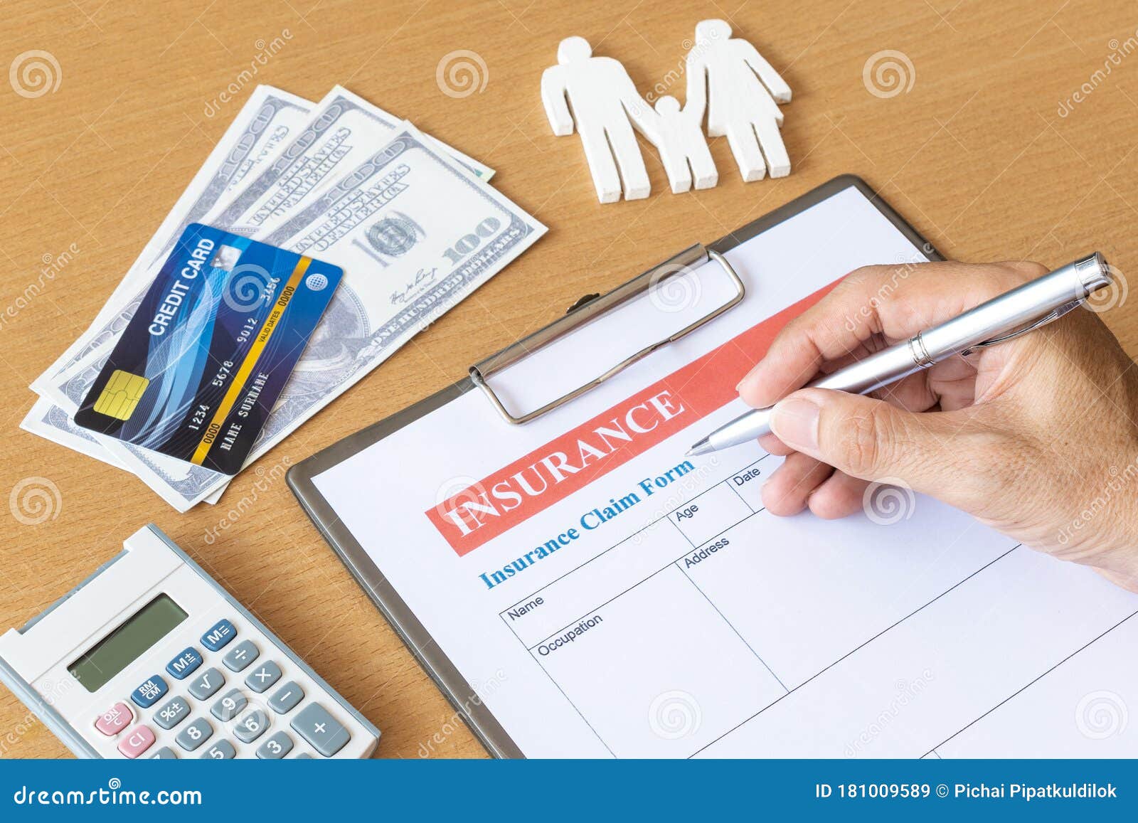  A person is filling out an insurance claim form with a pen while a calculator, credit card, and paper money are placed on the table.