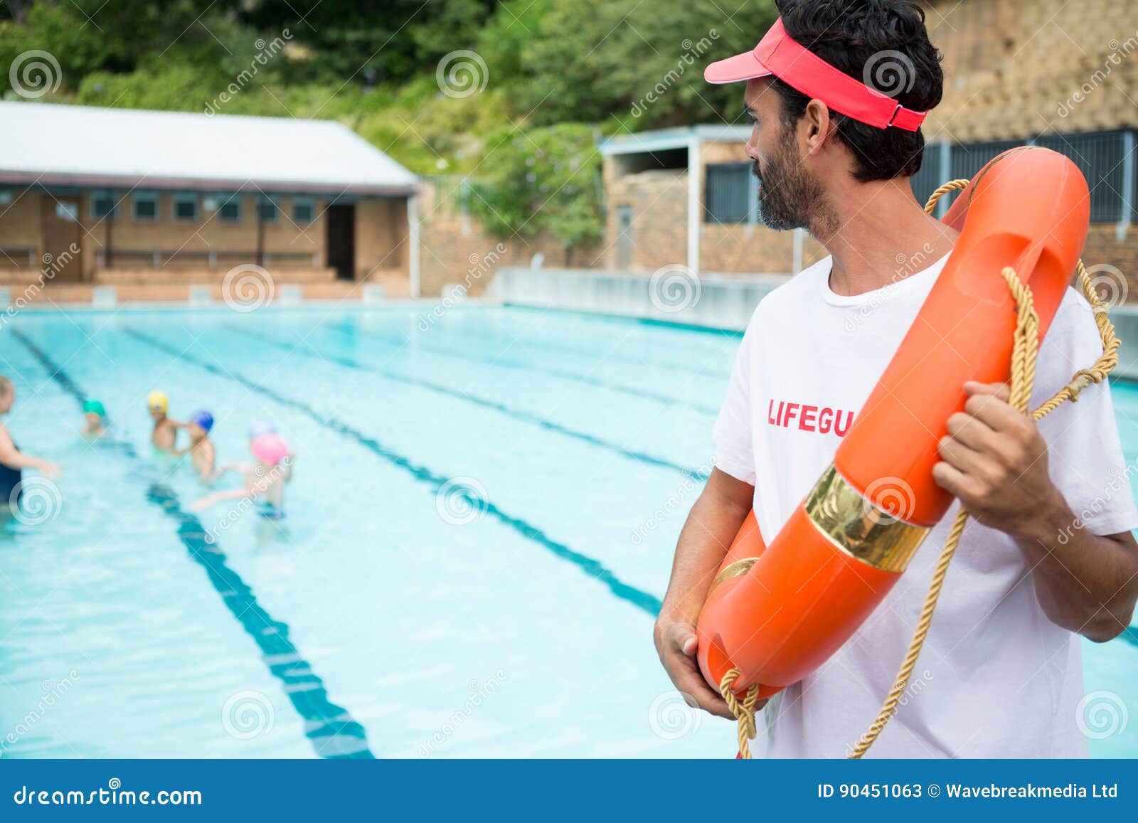 lifeguard with lifebuoy looking at students playing in the pool