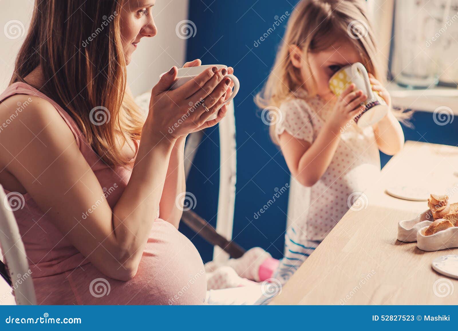 lifestyle capture of pregnant mother and baby girl having breakfast and drinking tea at home