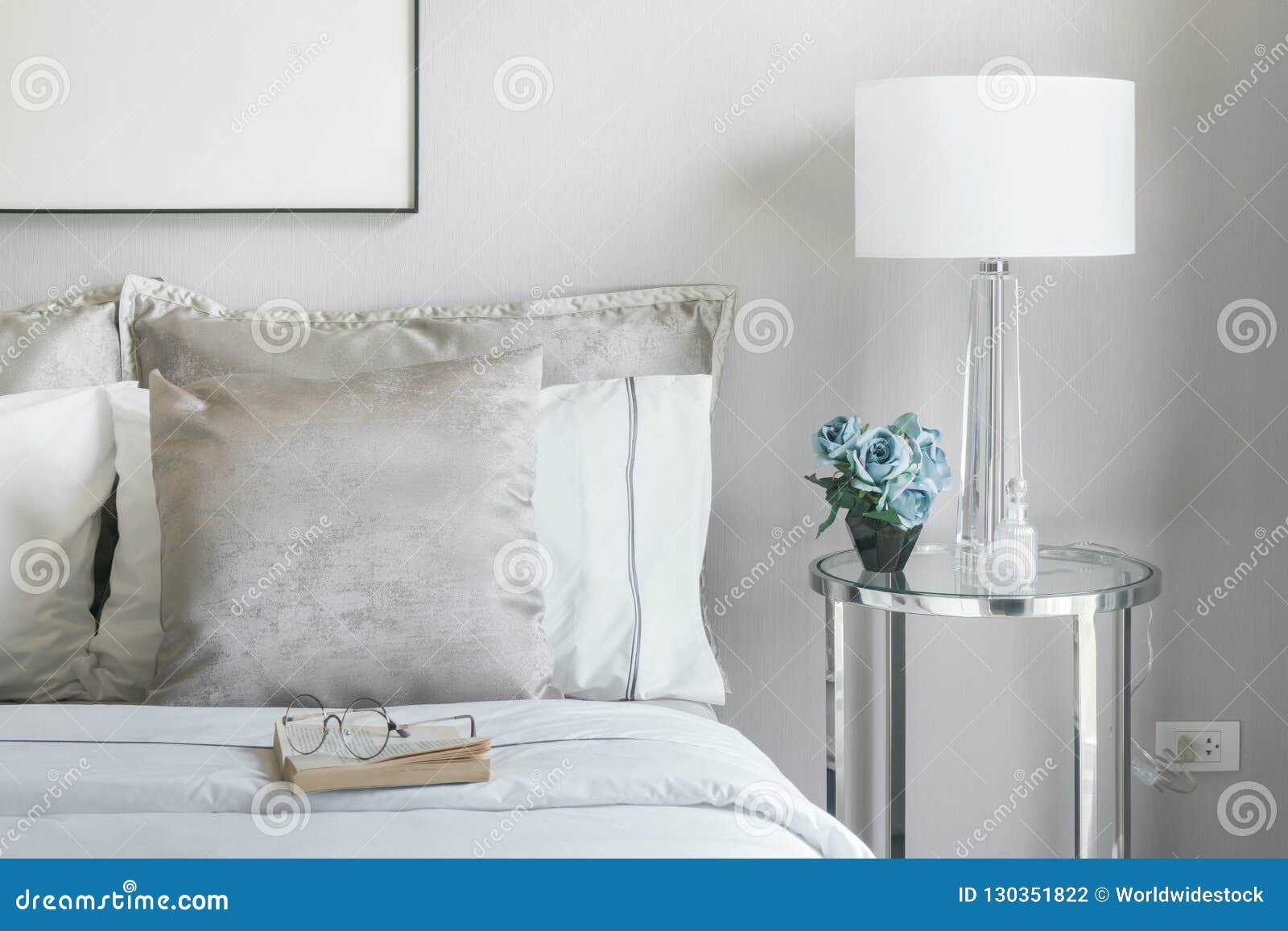 Light Gray and White Pillows on Bed with Flower Jar on Bedside Table