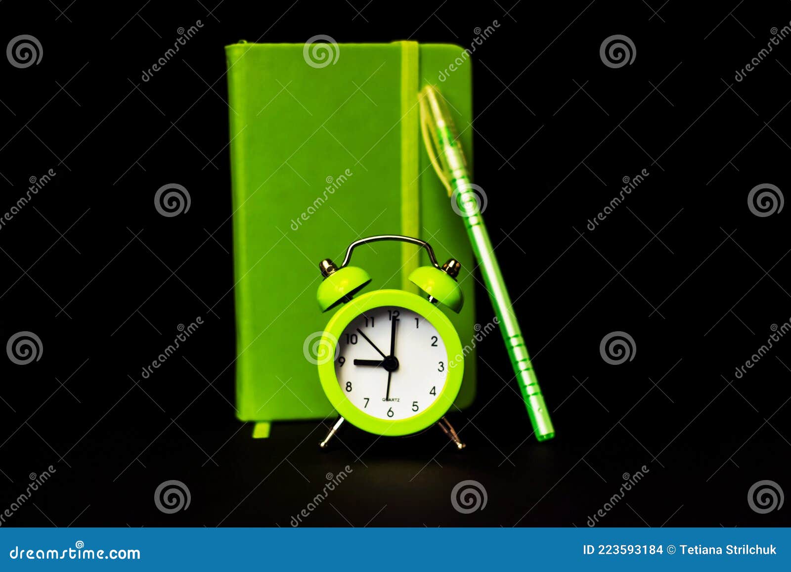 light green alarm clock on a black background. productivity conceptlight green notebook and pen. time minimalistic