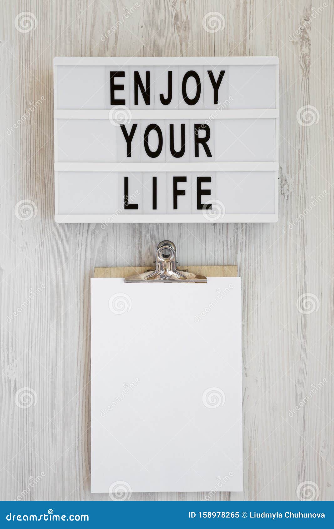 lightbox with text `enjoy your life`, noticepad with blank sheet of paper on a white wooden background, top view. overhead, from