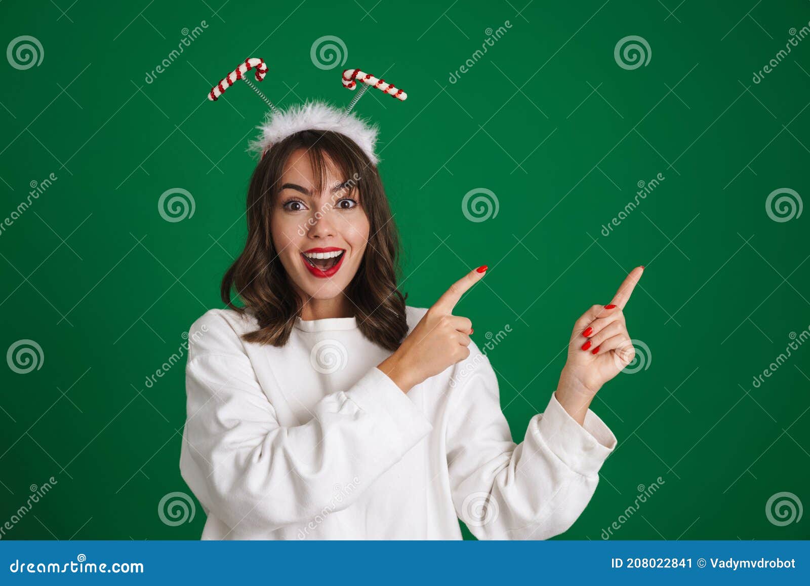 Linda garota vestindo chifres de brinquedo sorrindo e apontando dedos à parte. Linda garota excitada usando chifres de brinquedo sorrindo e apontando dedos à parte isolada sobre fundo verde
