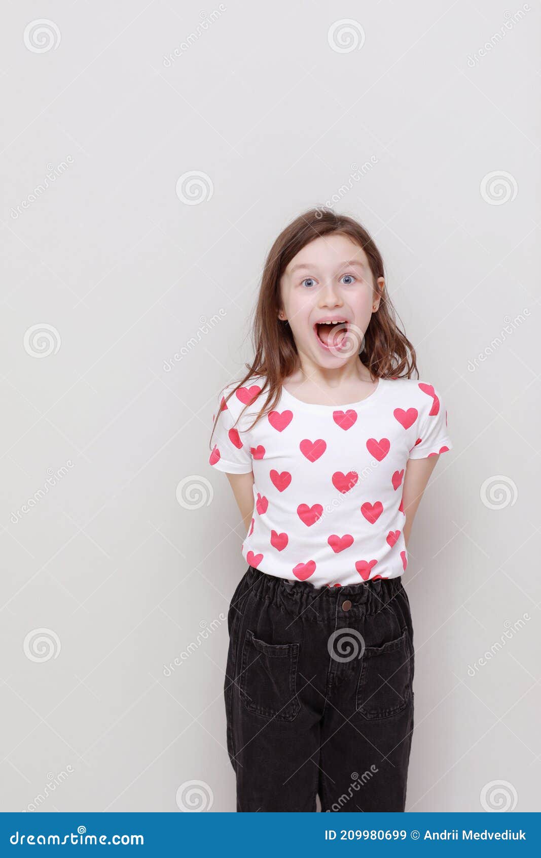 Linda Niña Sonriente En Camiseta Blanca Con Corazones Rojos Jeans Negros Abre Su Boca Ancha Sobre Fondo Blanco Imagen de - Imagen de lifestyle, publicidad: 209980699