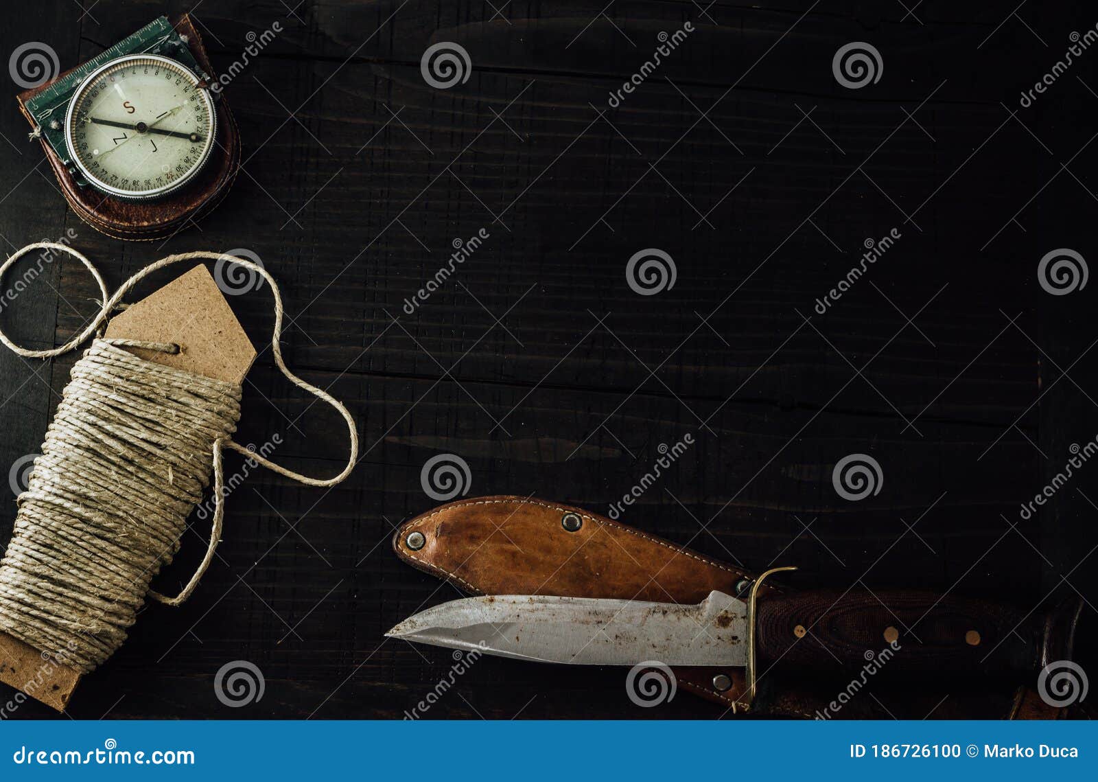 a linen rope, military compass and old hunting knife on the wooden table.