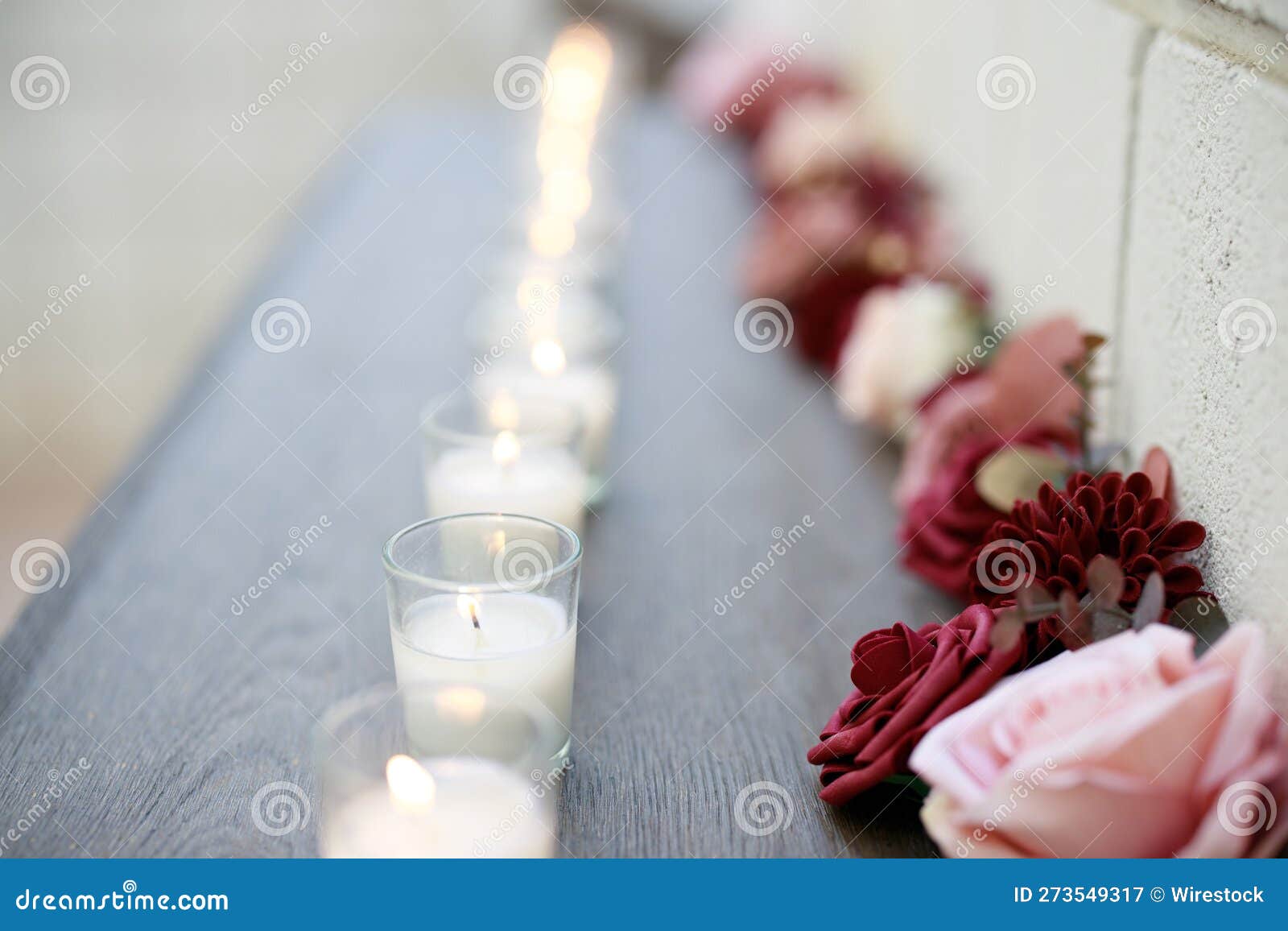 Lit Candles and Flowers Line a Shelf on a Table Outdoors Stock Image