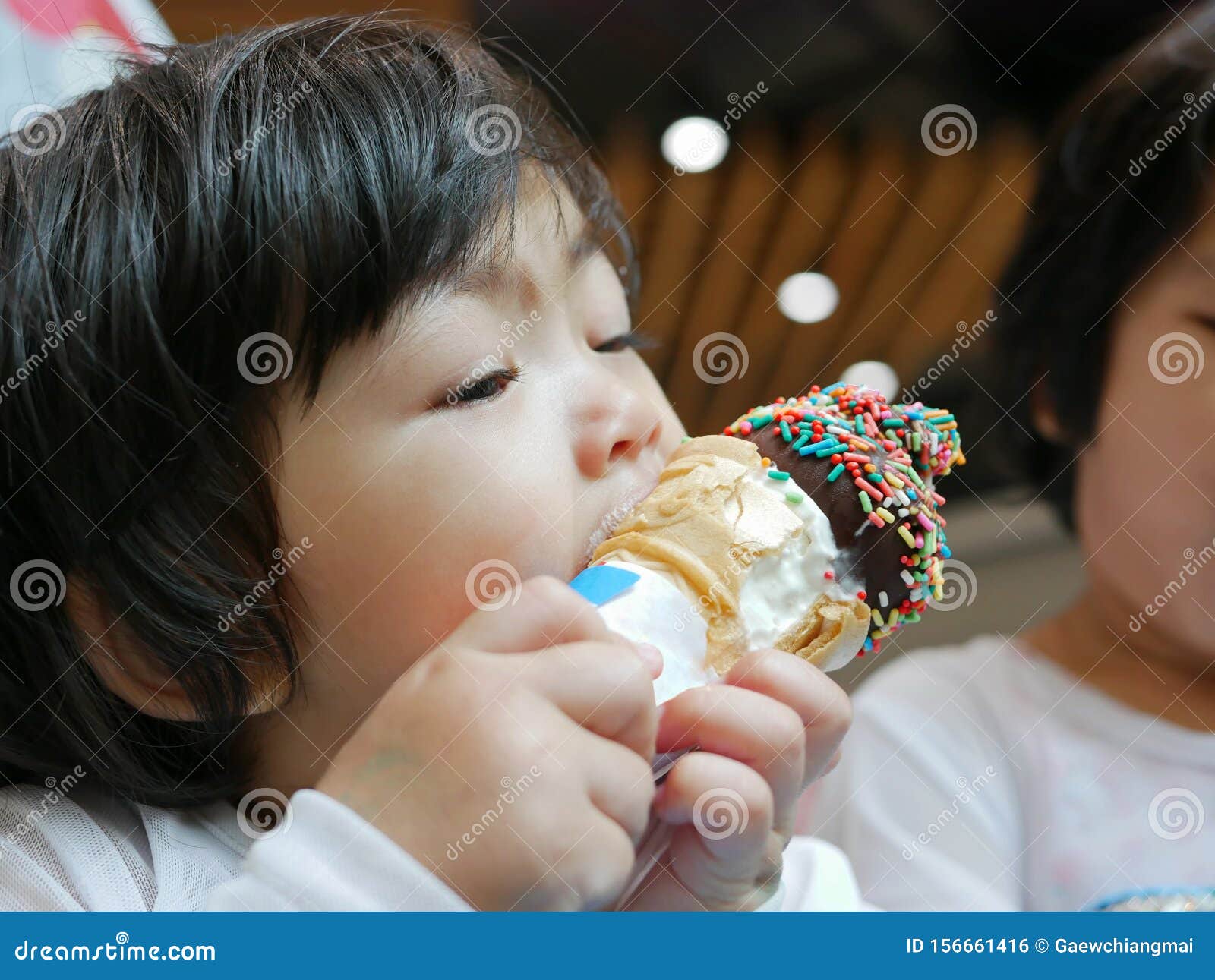 little asian baby girl, 2 years old, feeling blissful eating / biting ice cream cone - facial expression of joyfulness