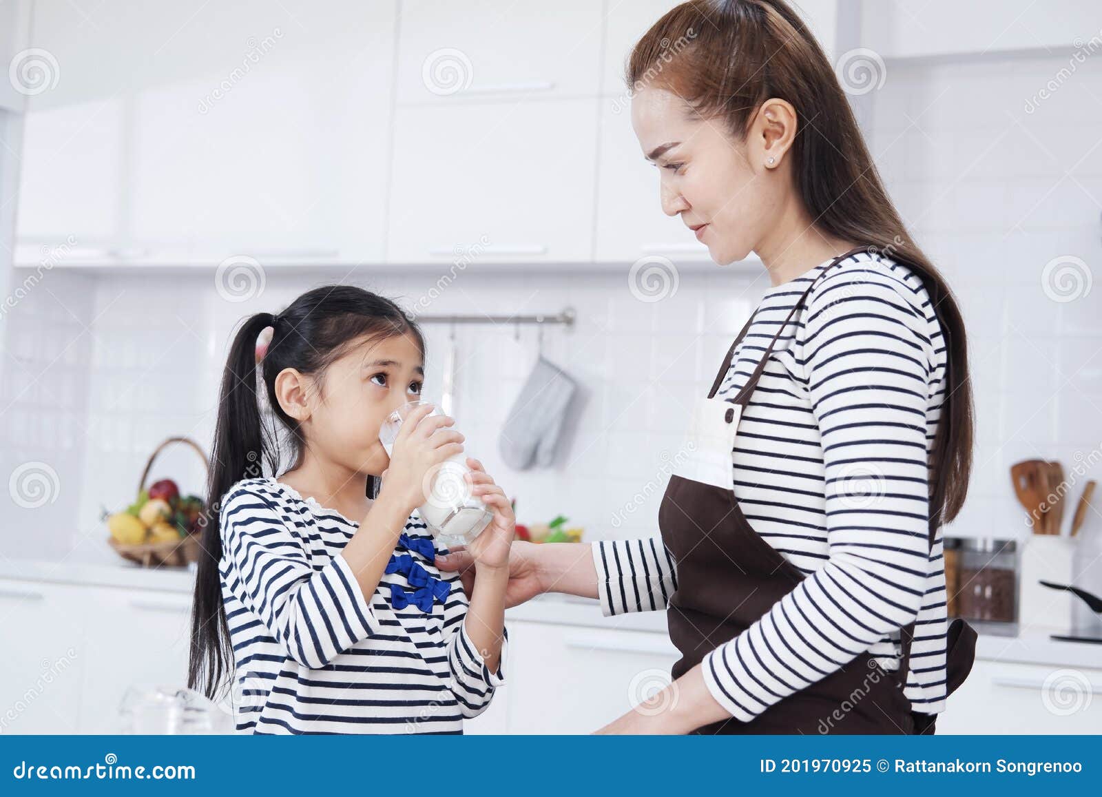 little asian girl child is drinking milk with mother in kitchen at home on holiday. family warmth and growth concept