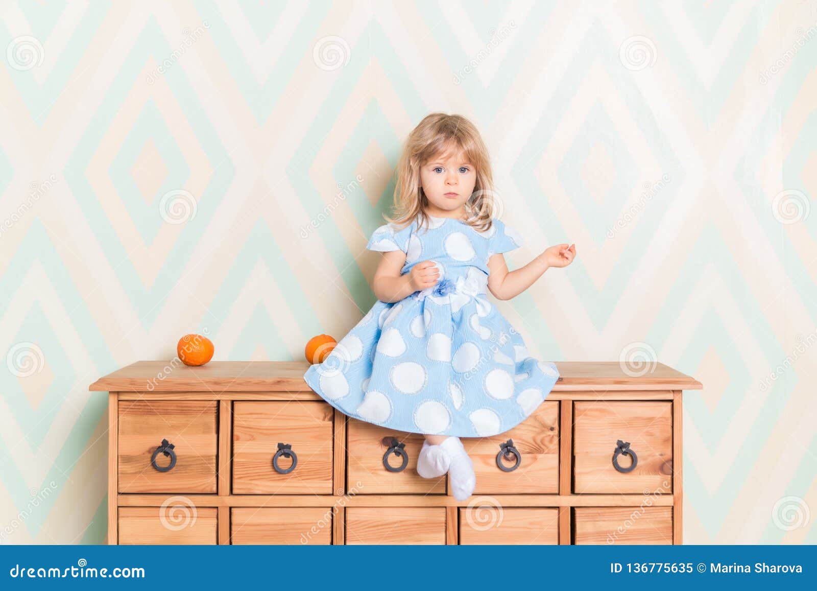 A Little Baby Girl In Her Room Sitting Cross Legged On Chest Of