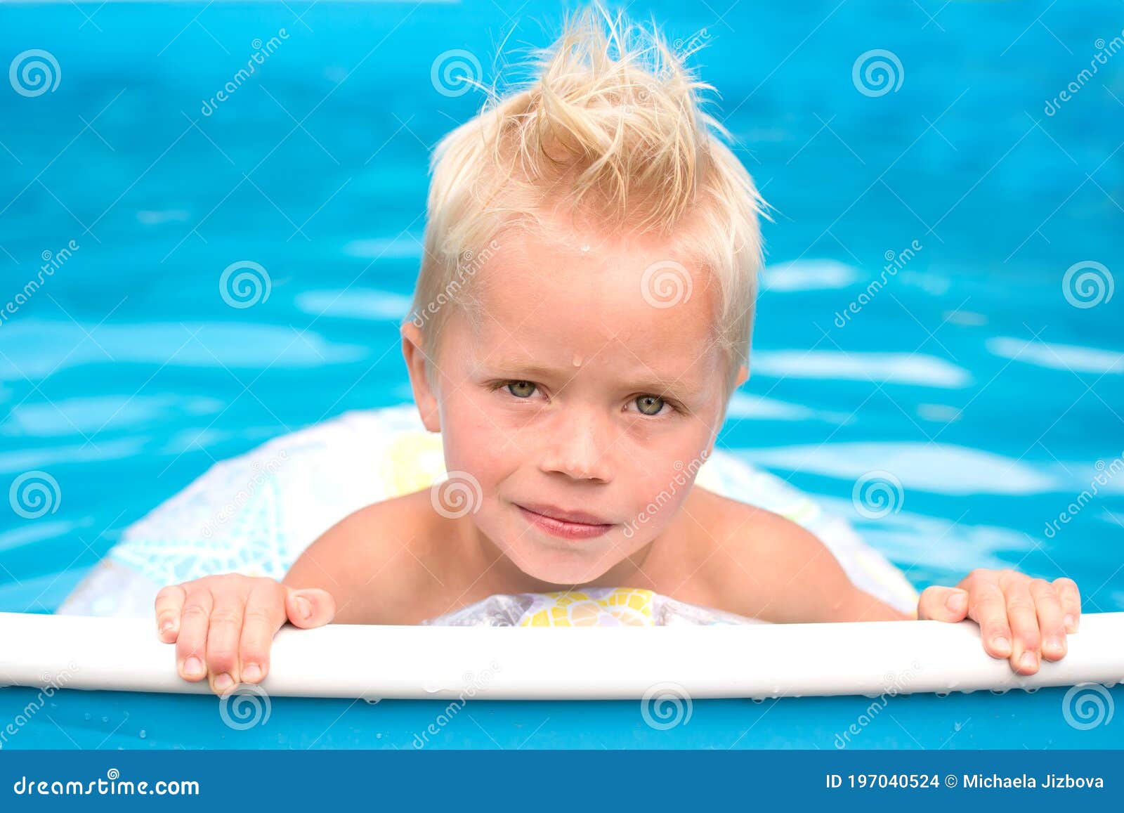 little blond boy is in swimming pool with inflable ring
