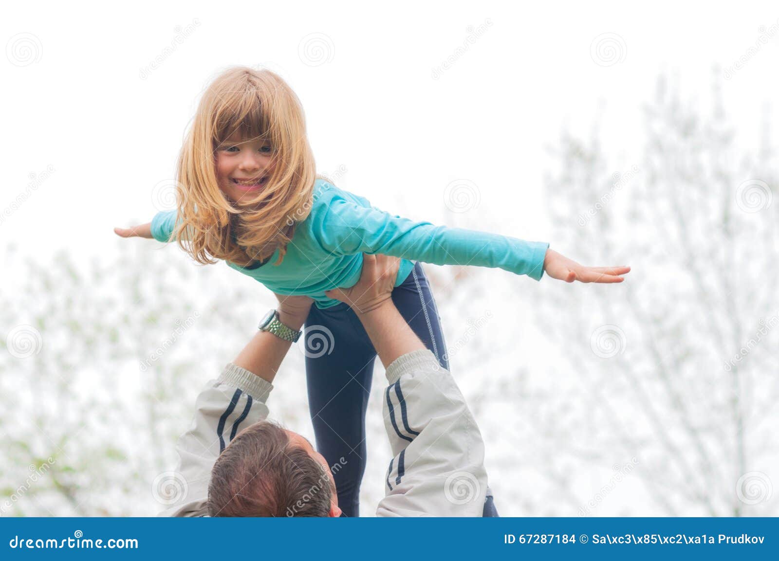 little blond girl lifted high in the air by her father outdoor