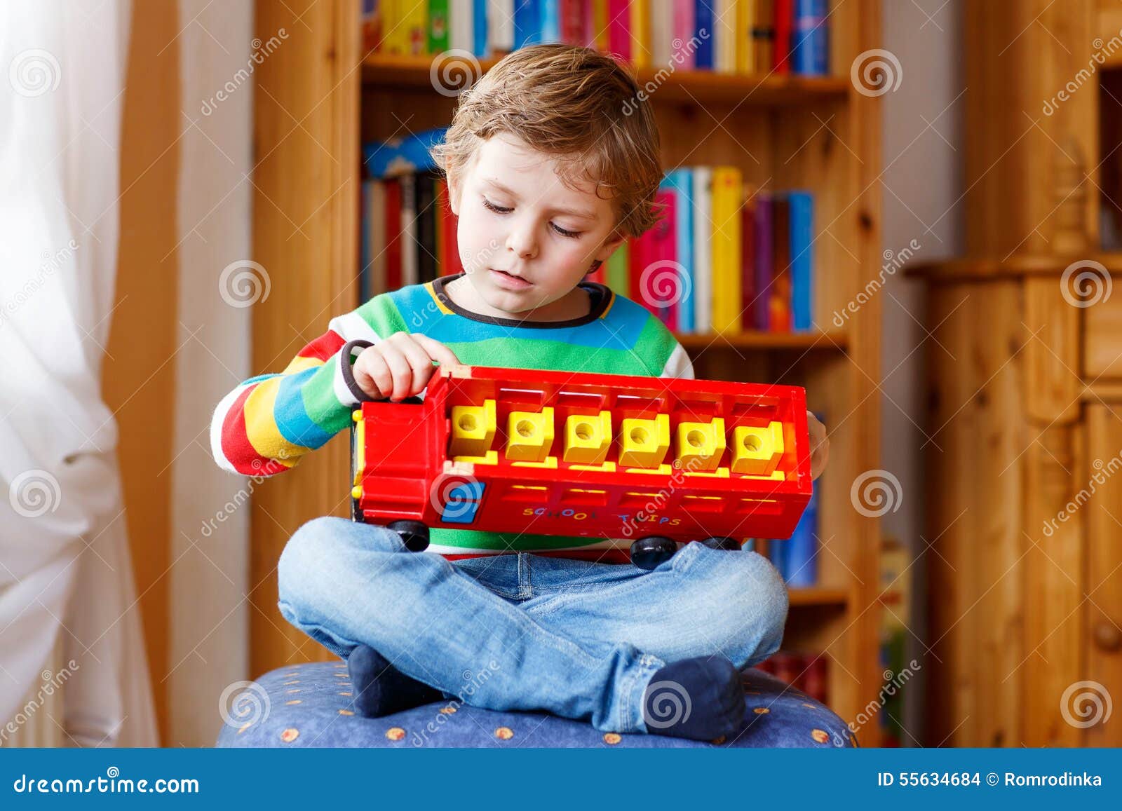 Little blond kid boy playing with wooden toy bus, indoors. Active kid boy playing with wooden toy bus, indoors. Child wearing colorful shirt. Portrait in a daycare.